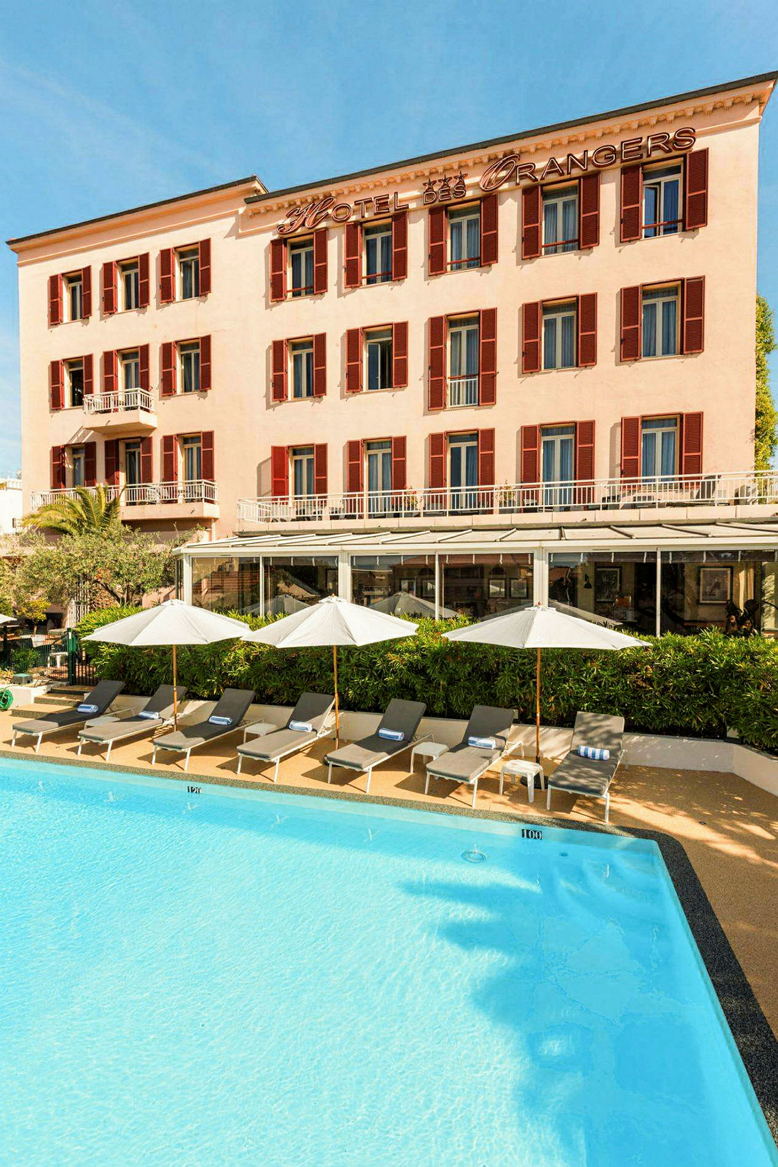 Hotelbygning med pool og liggestole. (AI-genereret tekst)