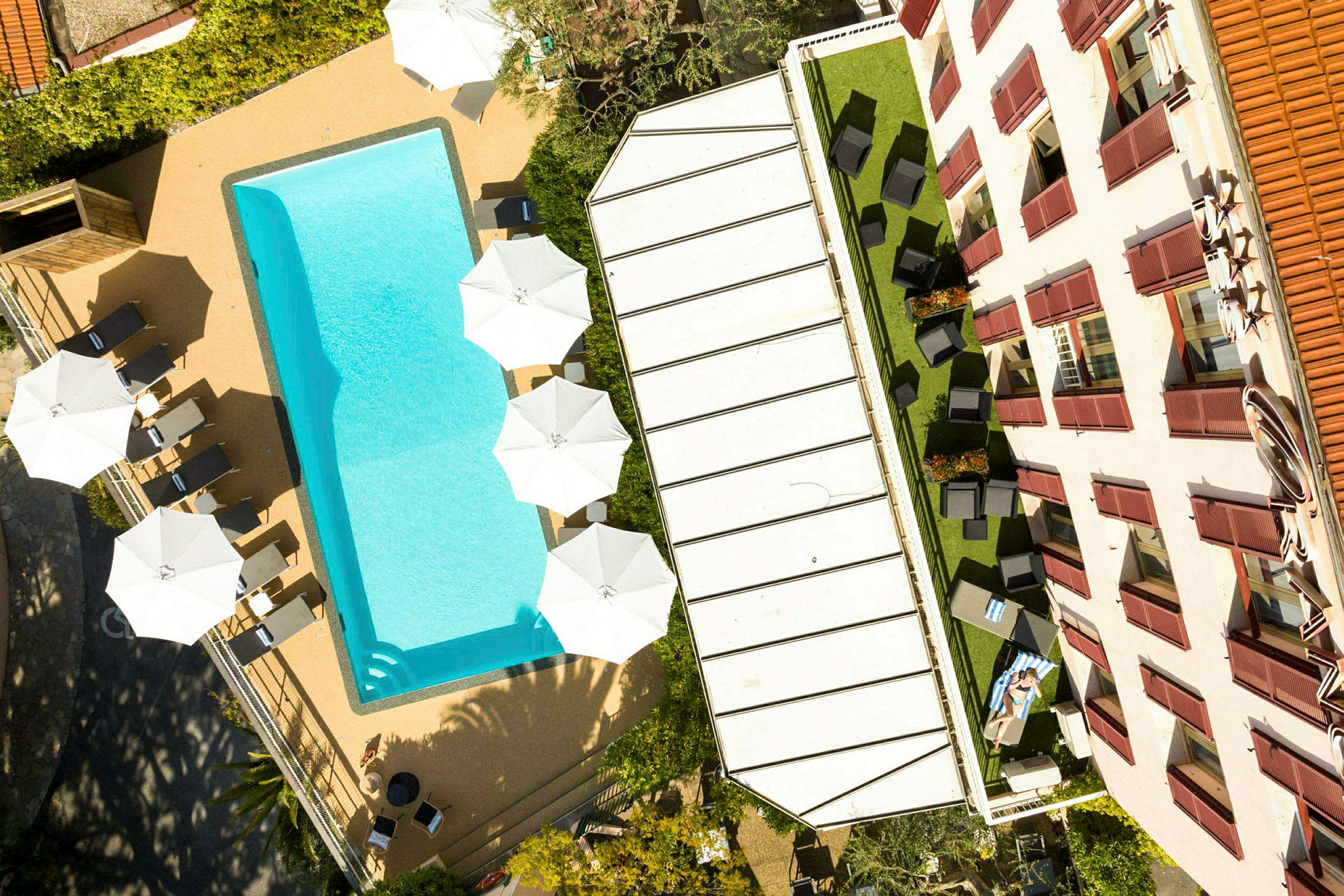 Billede af en pool, liggestole og parasoller ved siden af en bygning. (AI-genereret tekst)
