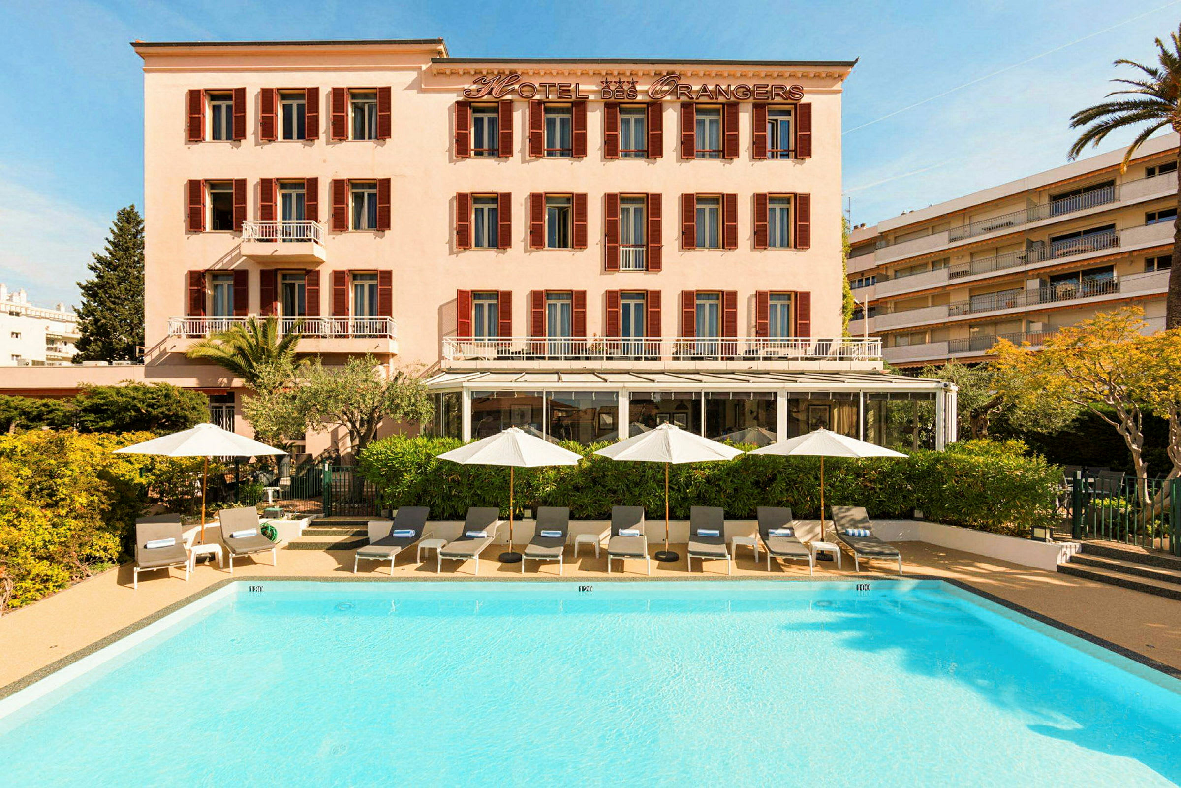 Hotelbygning med lys facade, solsenge og parasoller ved en udendørs pool. (AI-genereret tekst)