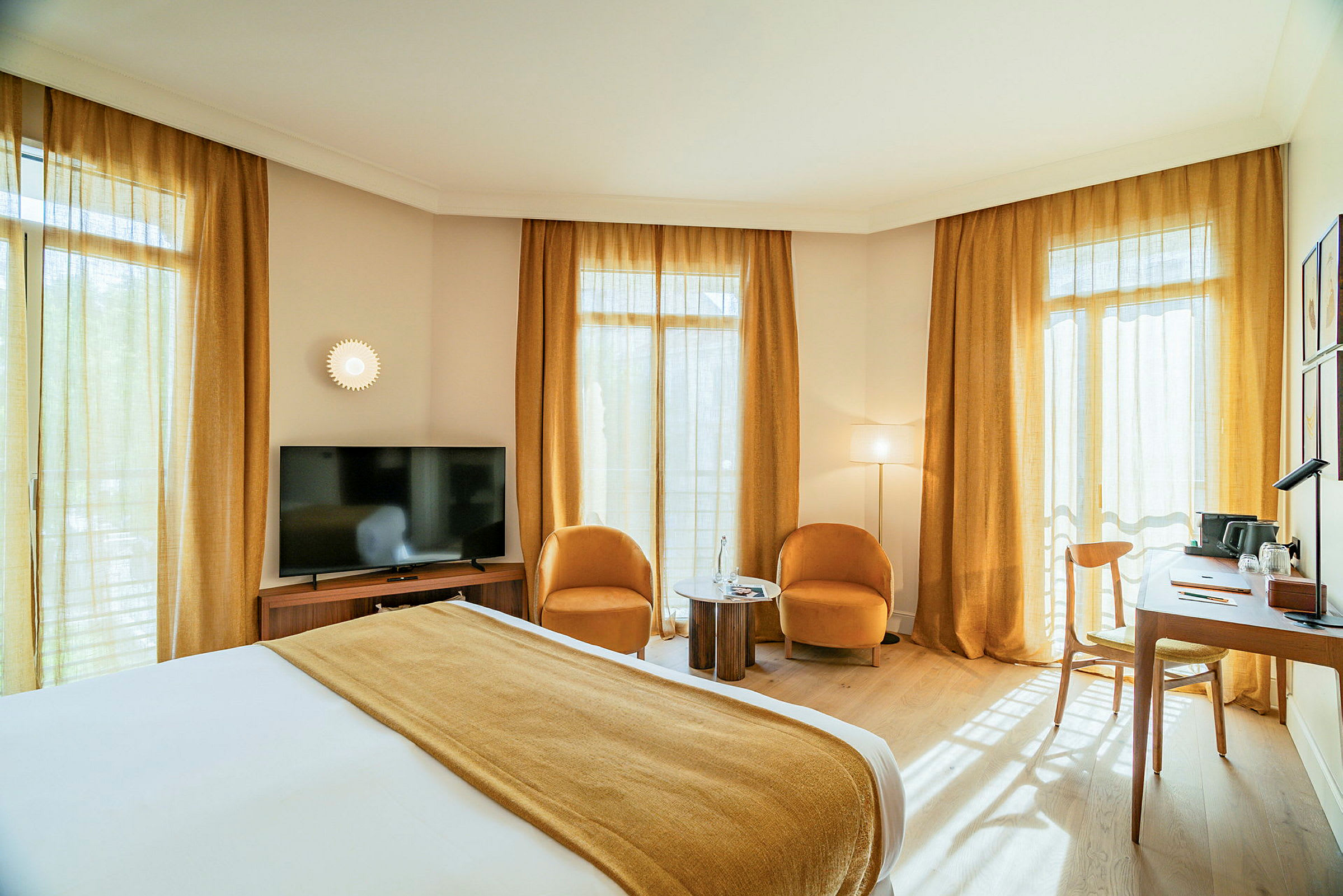 Et hotelværelse med en dobbeltseng, to lænestole og et lille bord, et fjernsyn og et skrivebord ved vinduerne. (AI-genereret tekst)