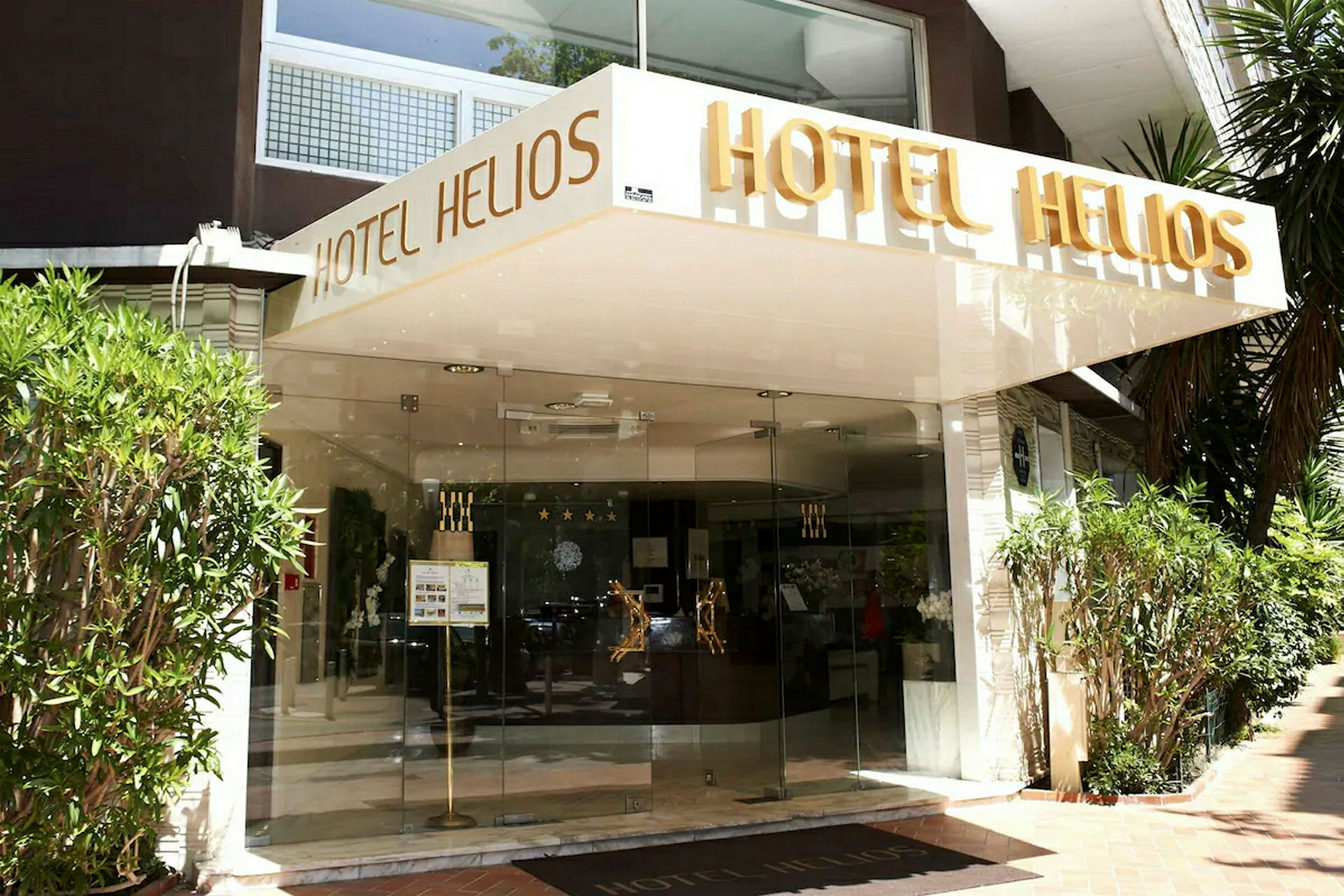 Indgangen til hotellet Hotel Helios med navnet skrevet over indgangen. (AI-genereret tekst)