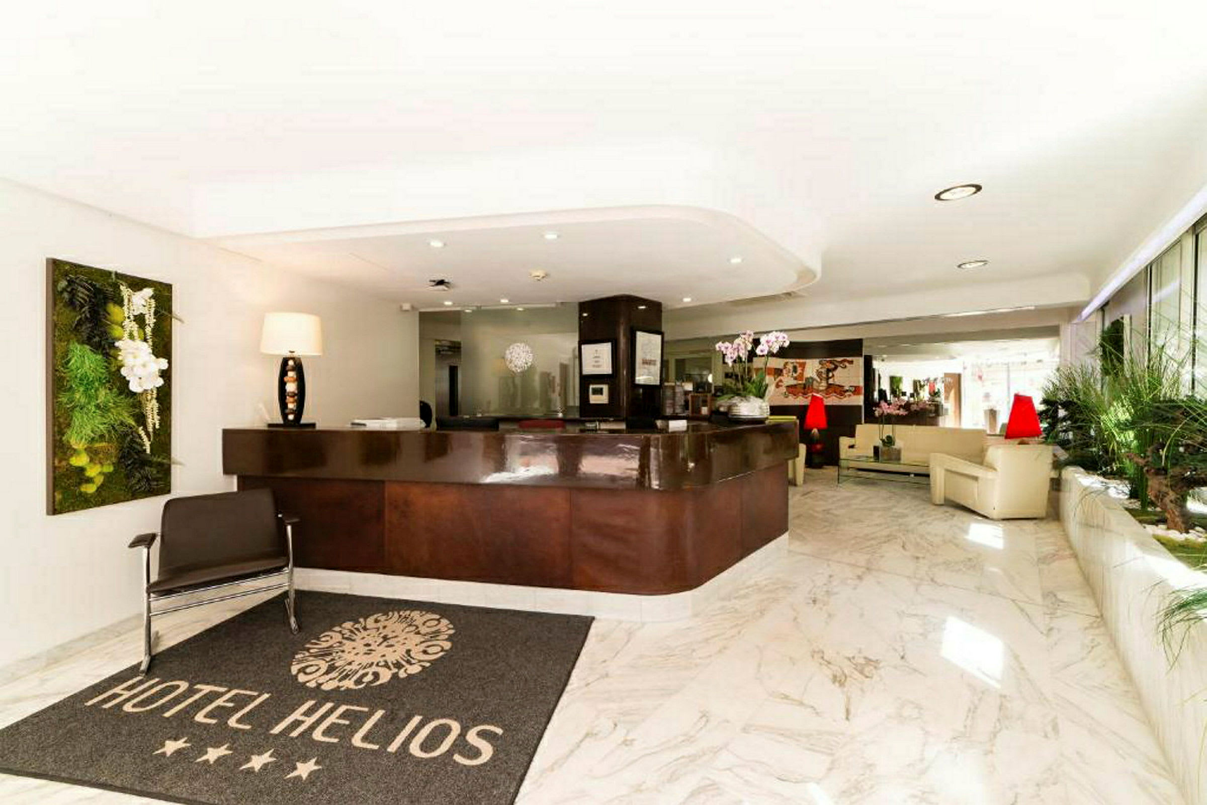 Hotellobby med reception, et tæppe med teksten "Hotel Helios" og siddeområder i lyse omgivelser. (AI-genereret tekst)