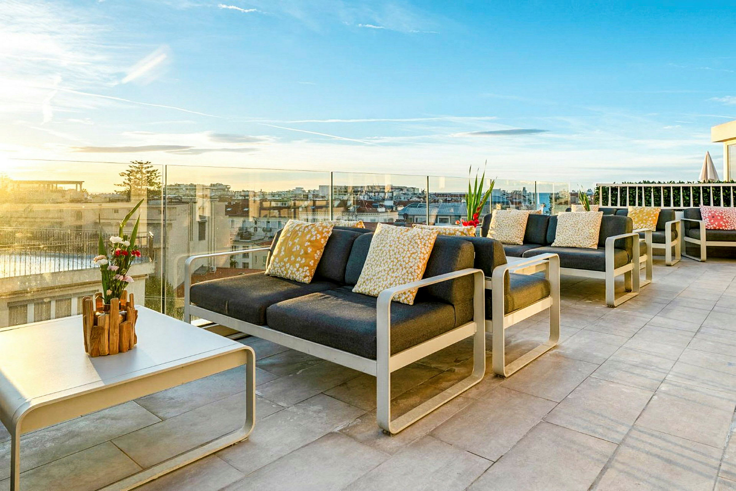 Møbleret tagterrasse med udsigt over byen og solnedgangen. (AI-genereret tekst)