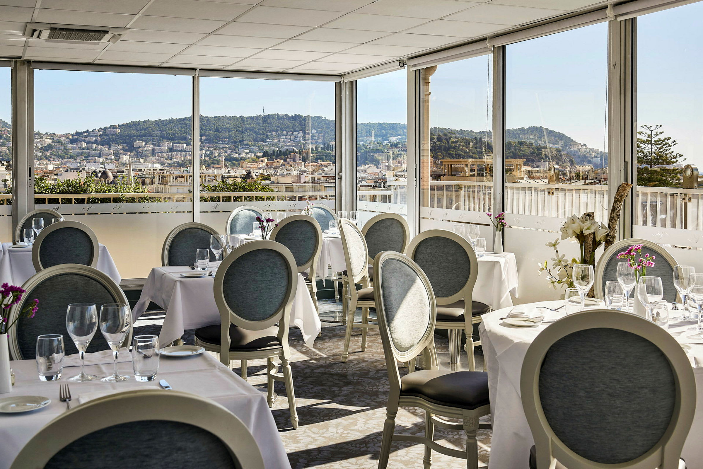 Restaurant med dækkede borde og udsigt over en by med bakker i baggrunden. (AI-genereret tekst)