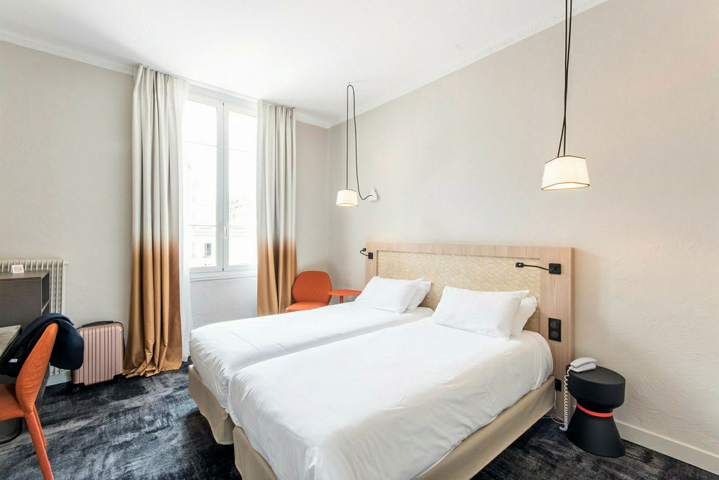 Et hotelværelse med to sammenkoblede enkeltsenge, et skrivebord, en stol og et vindue med lysindfald. (AI-genereret tekst)