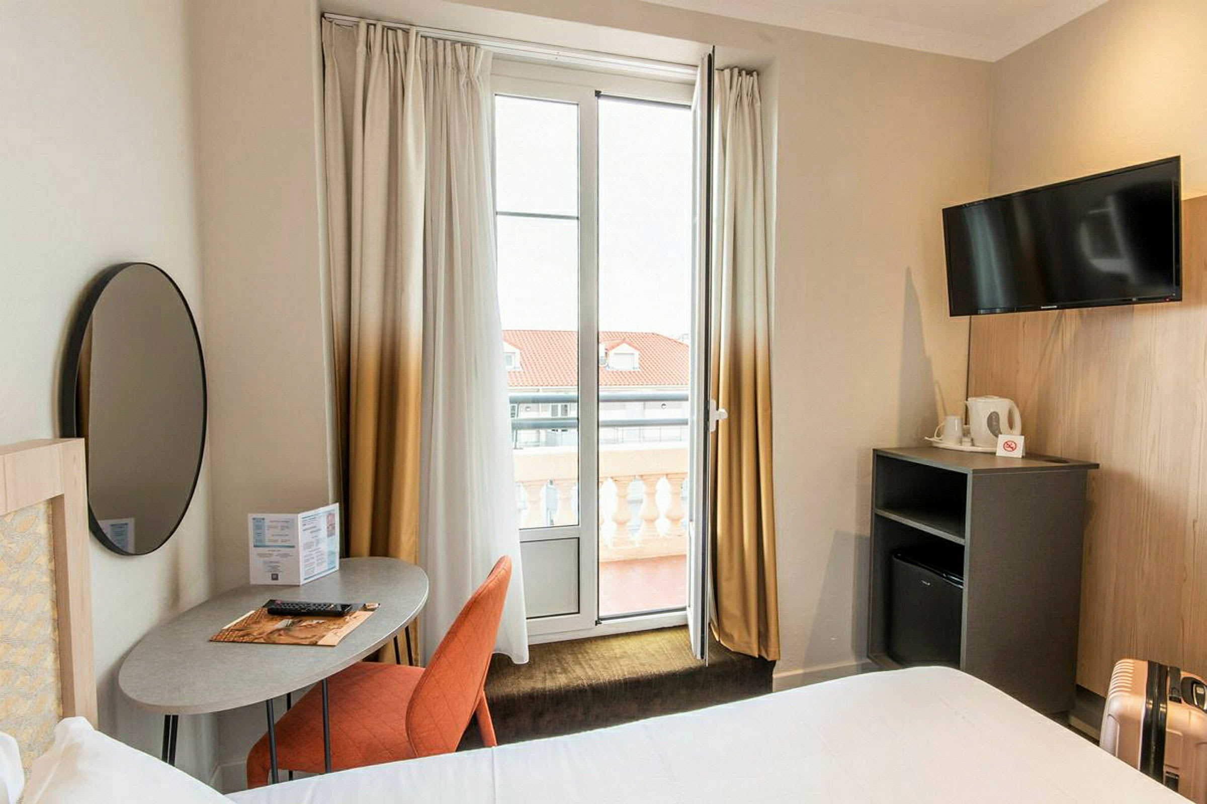 Et hotelværelse med moderne indretning, inklusive et skrivebord, en stol, en TV og en altan. (AI-genereret tekst)
