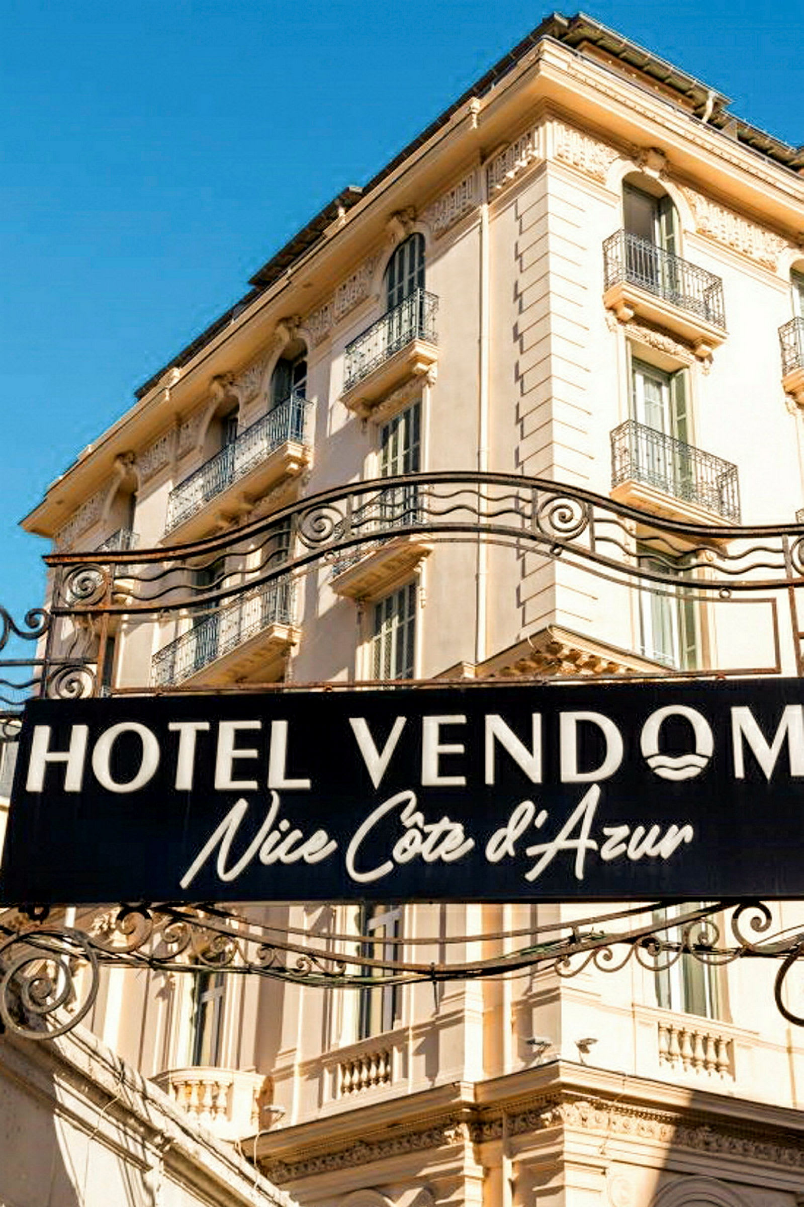 Skilt med teksten Hotel Vendome Nice Côte d’Azur foran en beige bygning. (AI-genereret tekst)