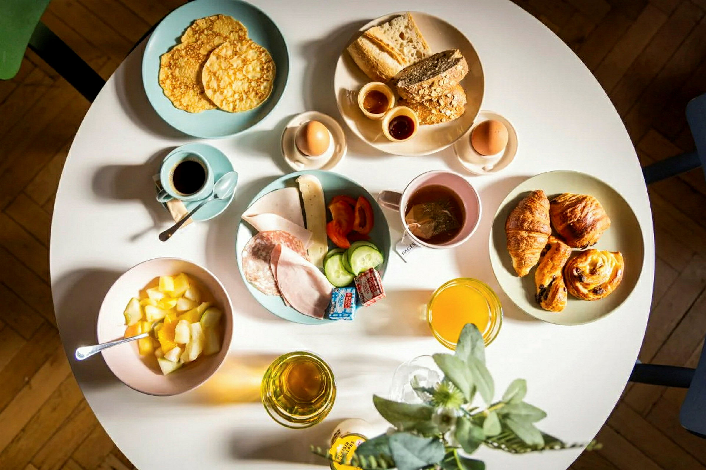 En morgenmadservering med brød, wienerbrød, æg, frugt, pålæg og drikke. (AI-genereret tekst)