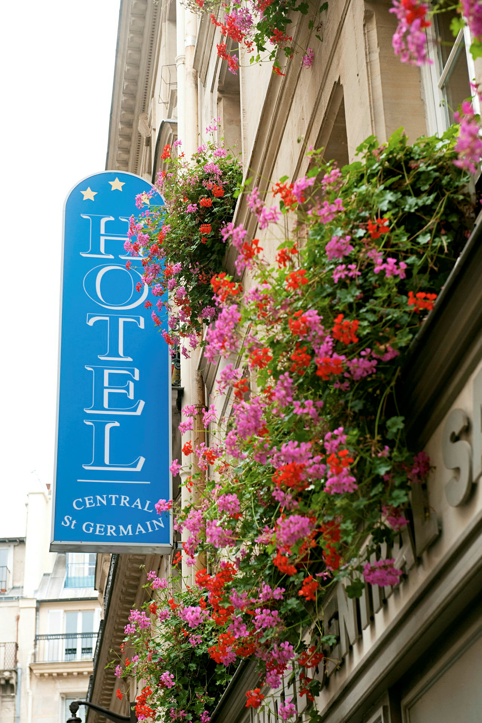 Et hotelskilt og en facade dekoreret med altankasser fyldt med røde og lyserøde blomster. (AI-genereret tekst)