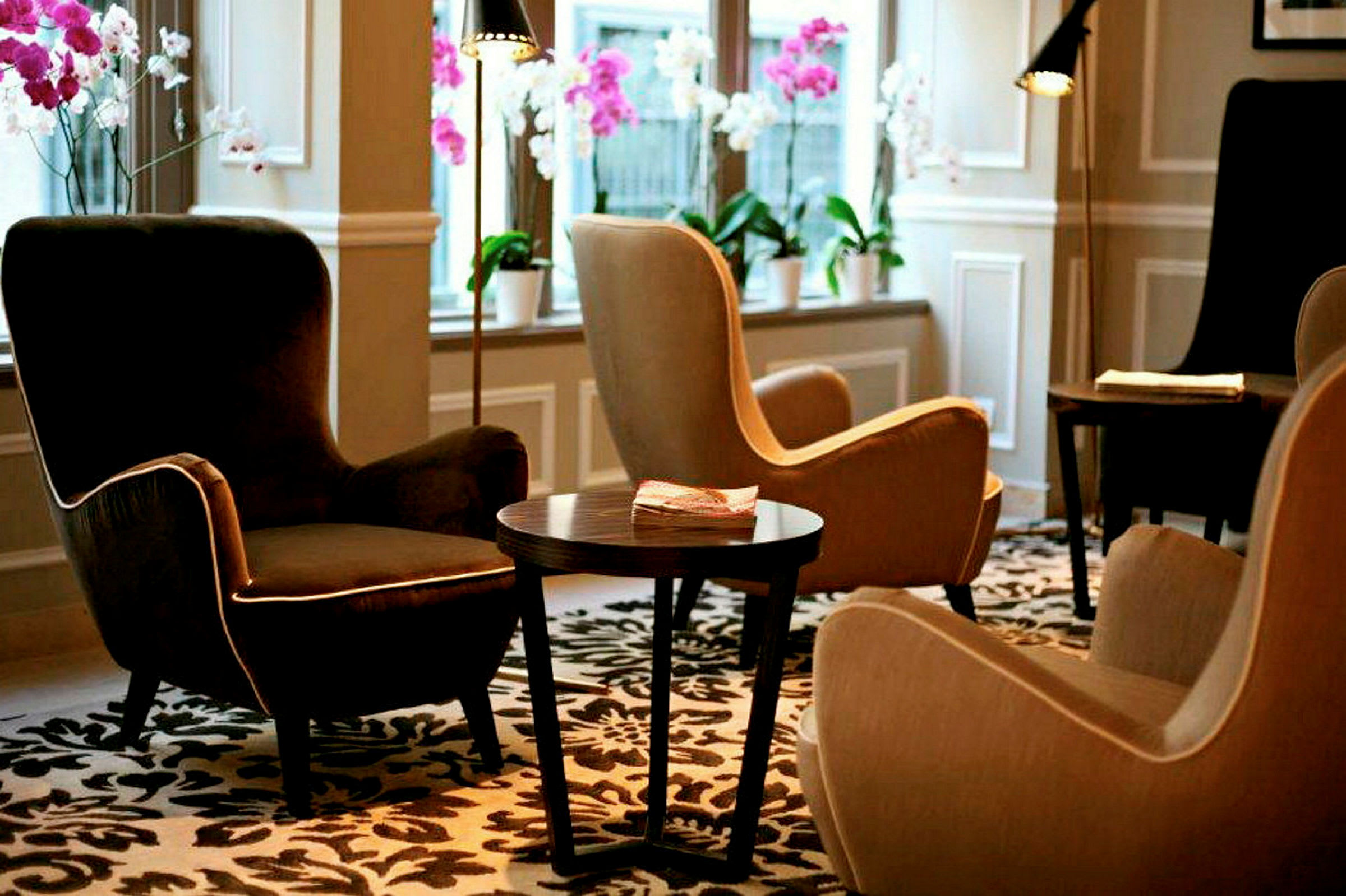 En lounge med komfortable lænestole, et bord og dekorative blomster i vinduerne. (AI-genereret tekst)