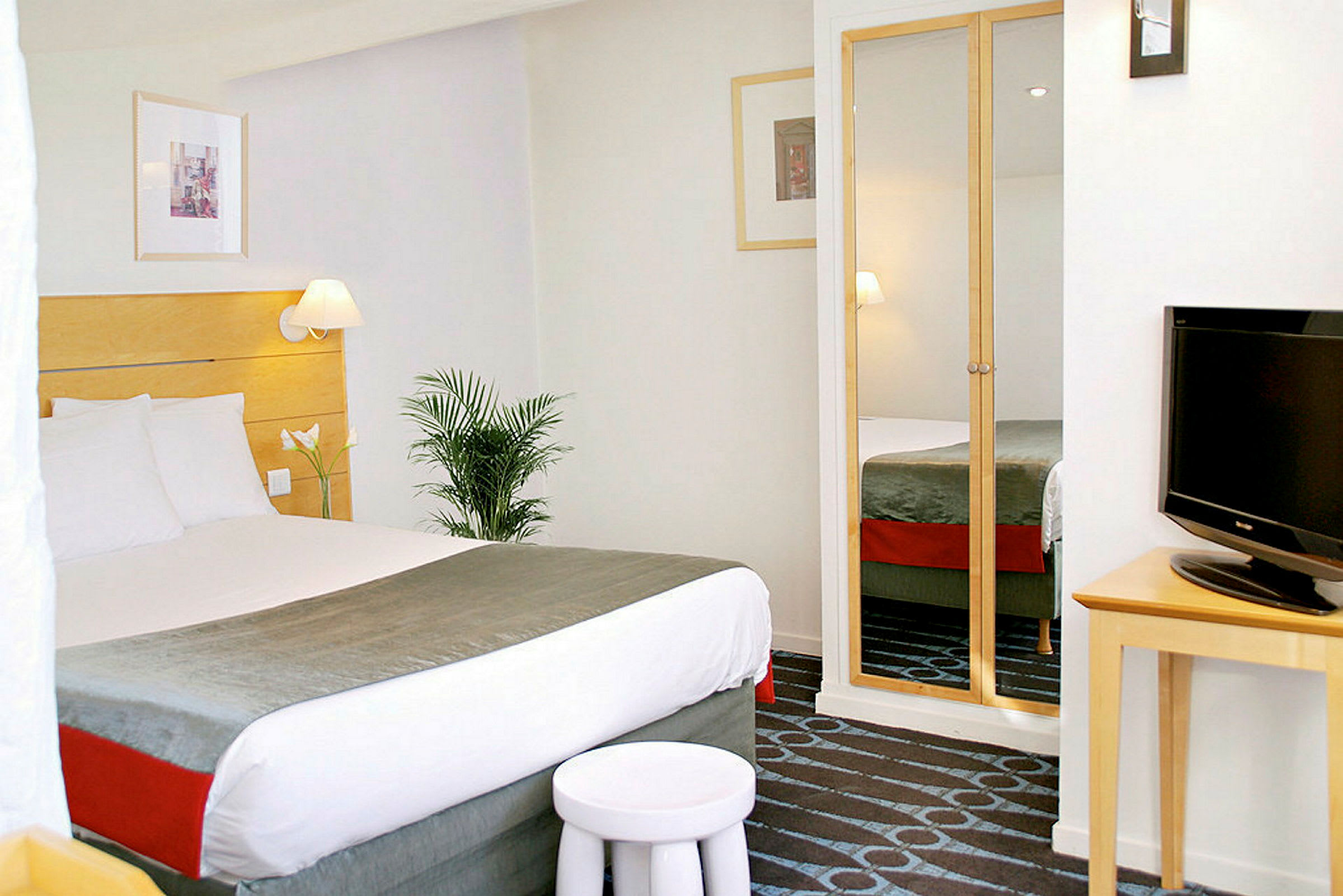 Hotelværelse med en redt dobbeltseng, fjernsyn og garderobe med spejldøre. (AI-genereret tekst)