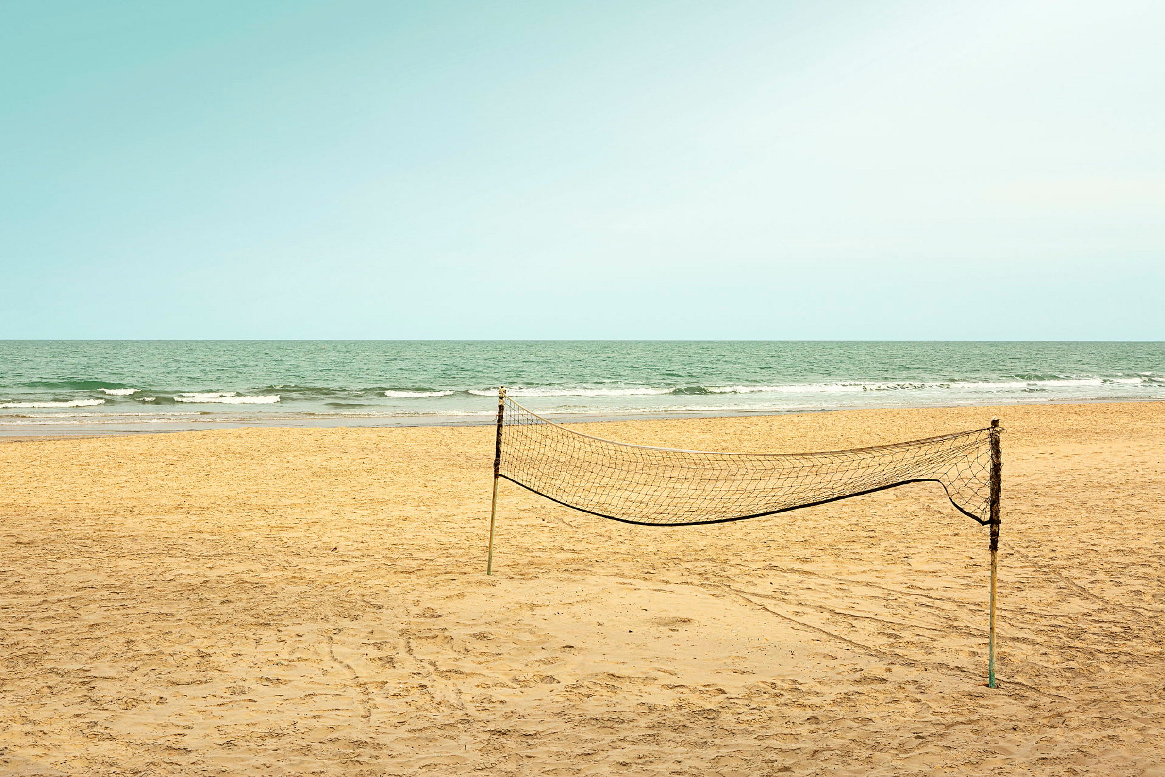En tom sandstrand med et opstillet volleyballnet og havet i baggrunden. (AI-genereret tekst)