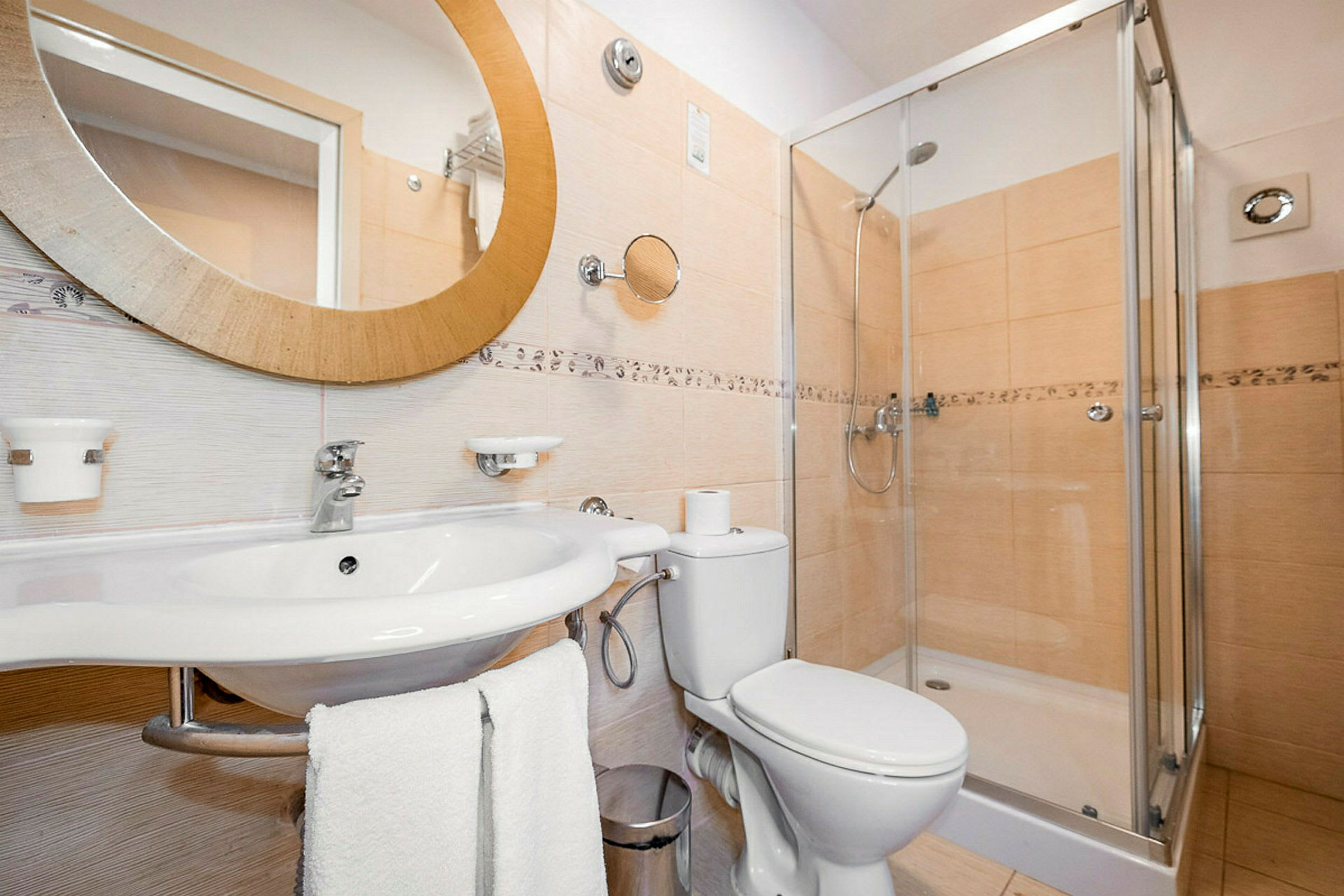 Et badeværelse med en hvid vask, rundt spejl, toilet og en brusekabine. (AI-genereret tekst)