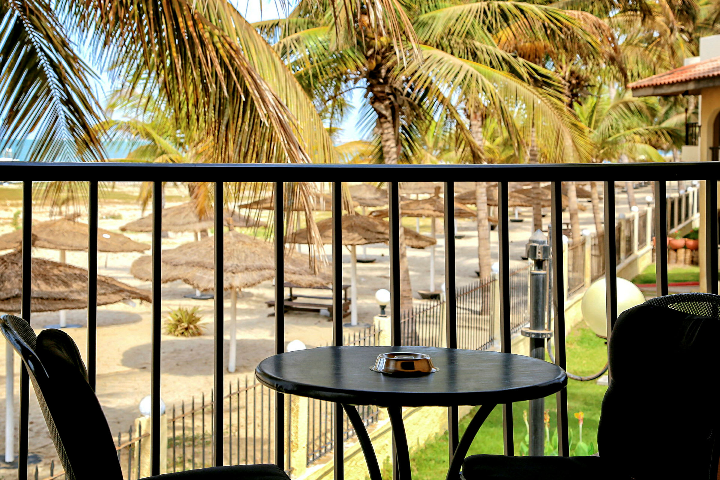 Et bord med to stole på en terrasse med udsigt over en have med palmer og parasoller ved stranden. (AI-genereret tekst)