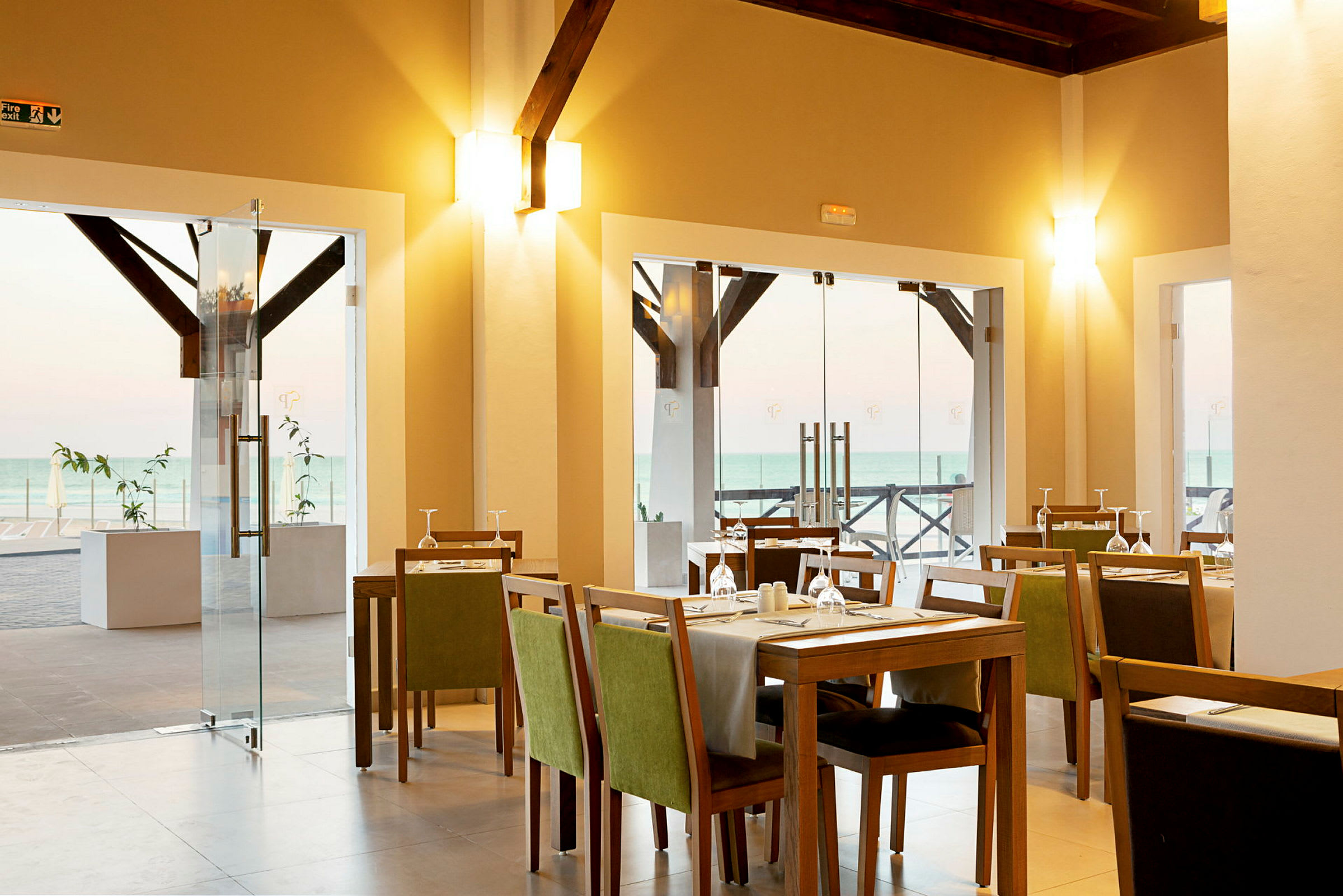 En restaurant med borde, stole og duge samt glasdøre med udsigt til havet udenfor. (AI-genereret tekst)