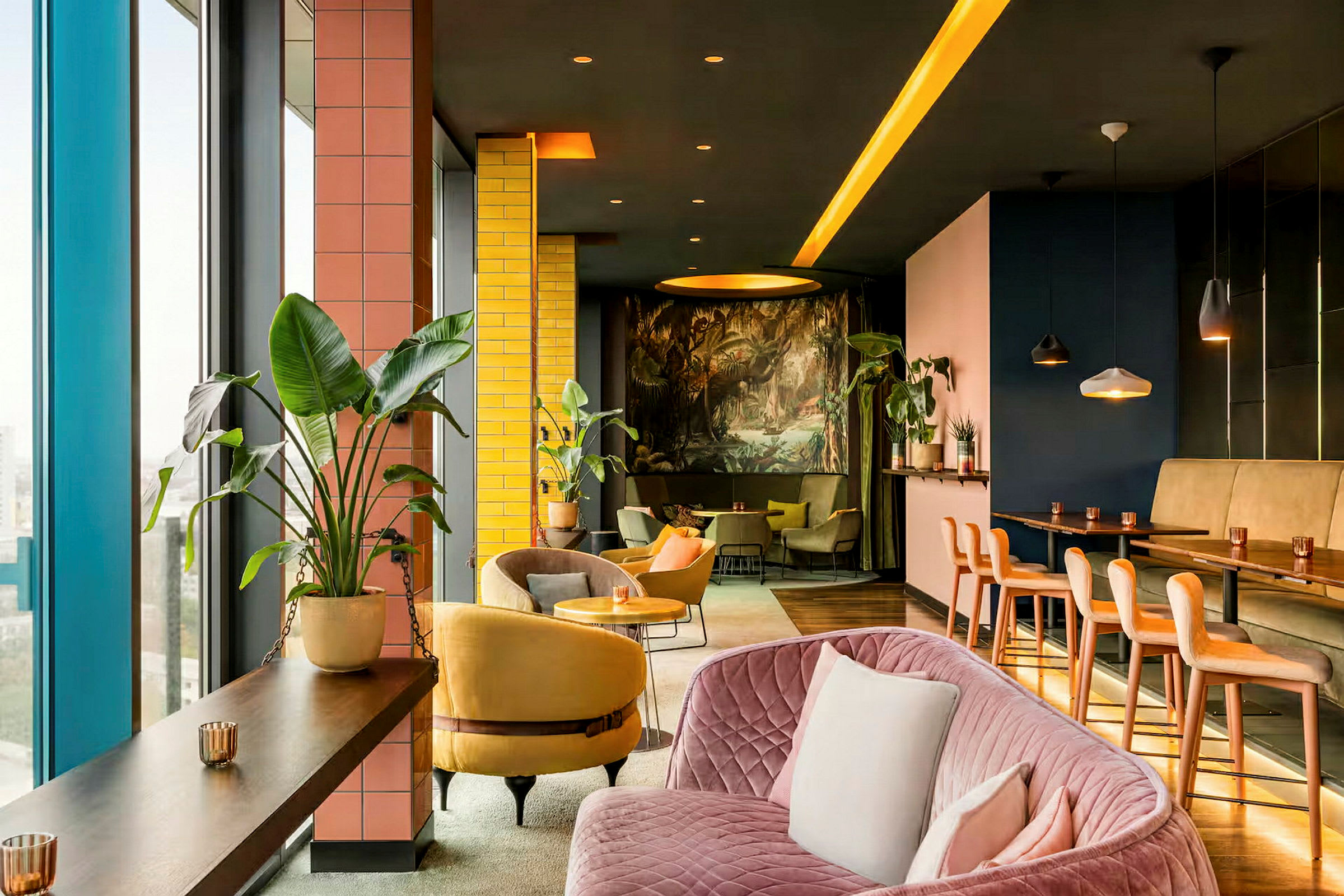 Interiør af et moderne og farverigt loungemiljø med planter, sofaer og stole samt et højbordsområde. (AI-genereret tekst)