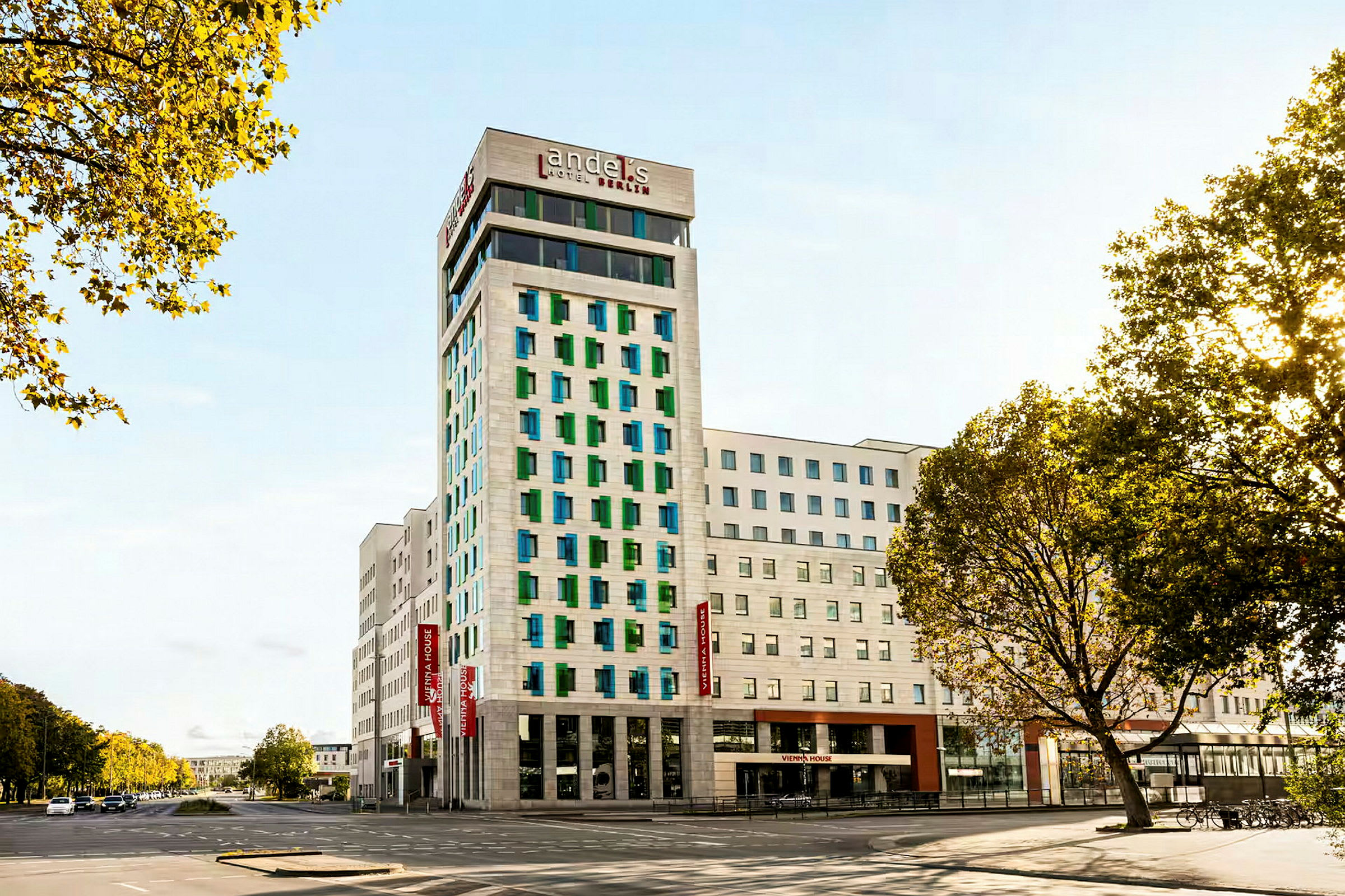 En moderne hotelbygning med hvid facade og farvede vinduer, omgivet af veje og træer. (AI-genereret tekst)