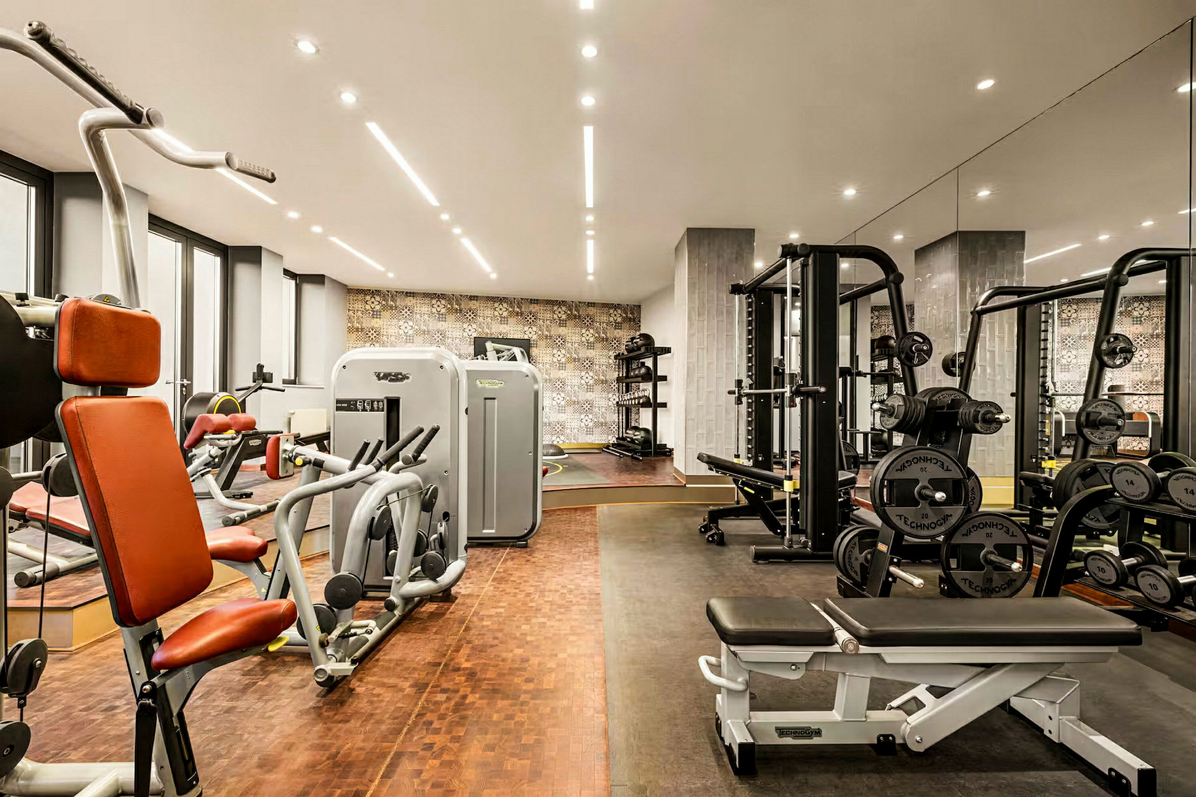 Et fitnessrum udstyret med forskellige træningsmaskiner, frie vægte og bænke, med spejlbeklædte vægge og moderne belysning. (AI-genereret tekst)