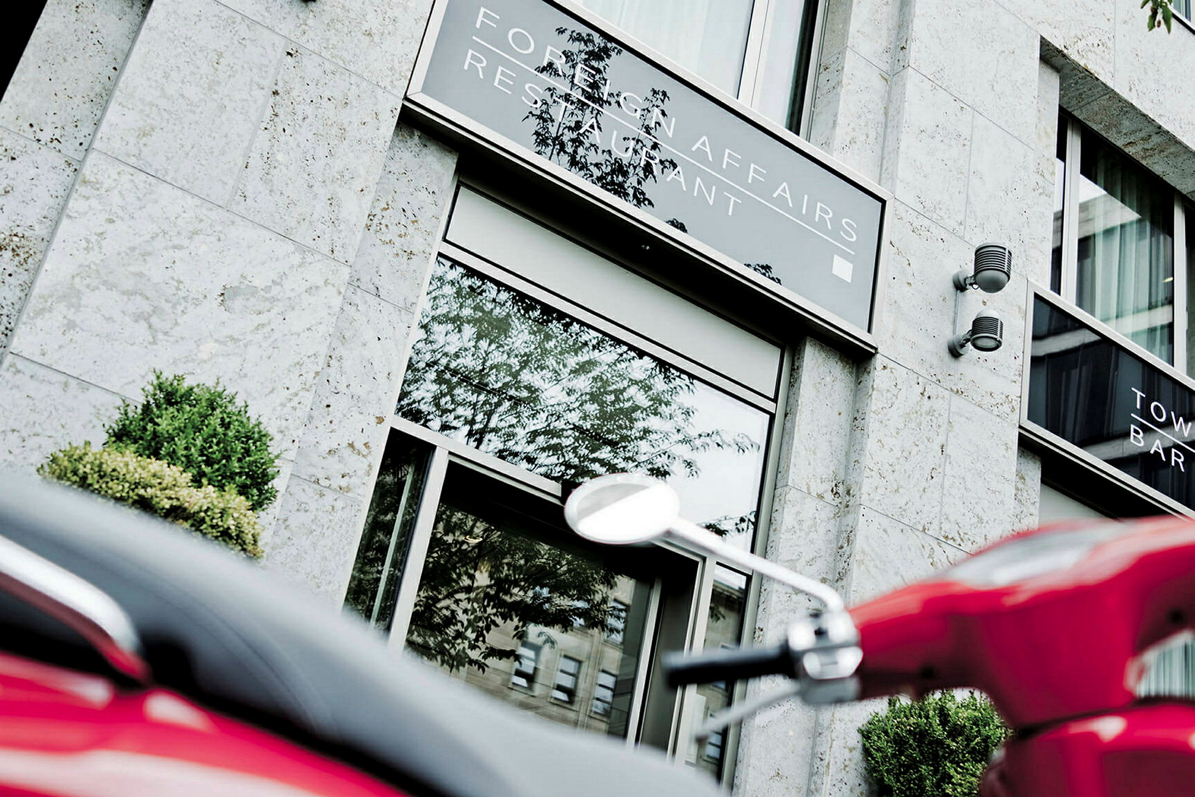 En moderne bygning med skilte for en restaurant og en bar, hvor en rød scooter ses i forgrunden. (AI-genereret tekst)