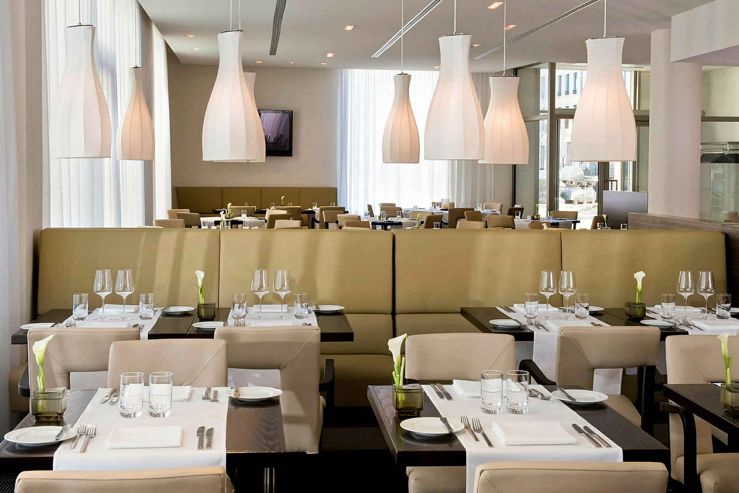 En restaurant med moderne møbler og dækkede borde. Lyse hængende lamper ses i loftet. (AI-genereret tekst)