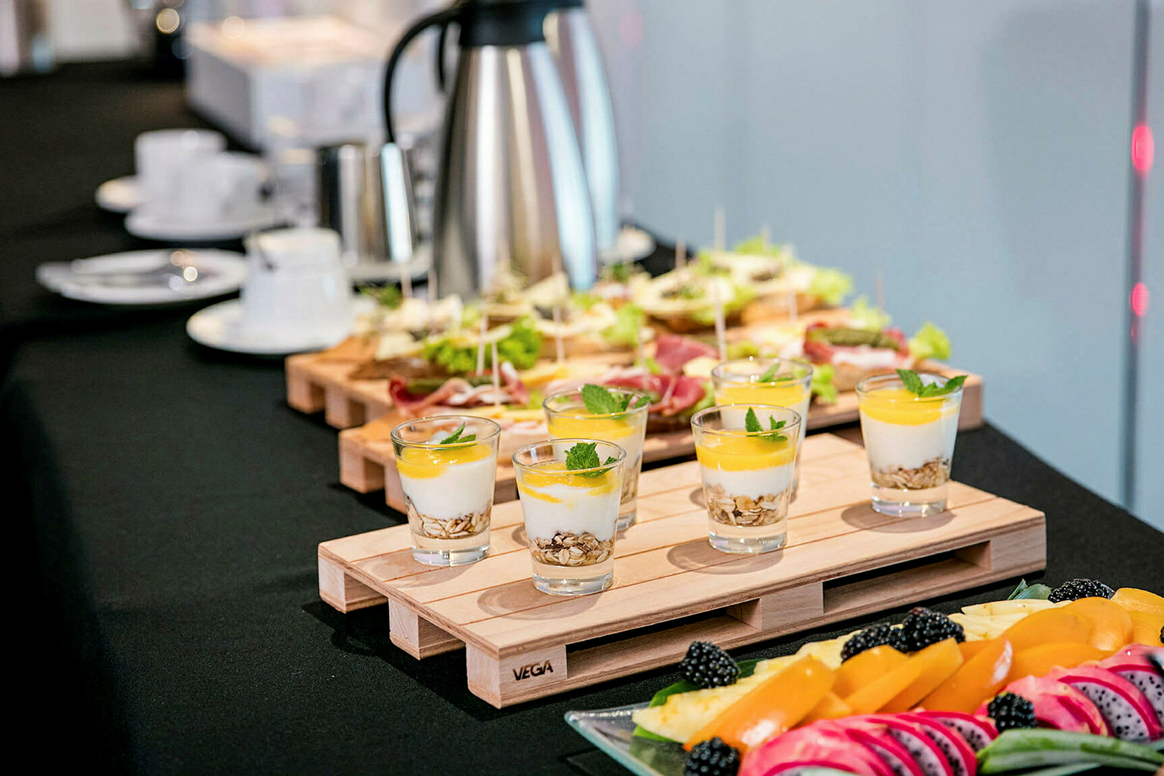 Et bord med forskellige madvarer, herunder glas med yoghurt og frugt, smørrebrød samt et fad med frisk frugt og bær. (AI-genereret tekst)