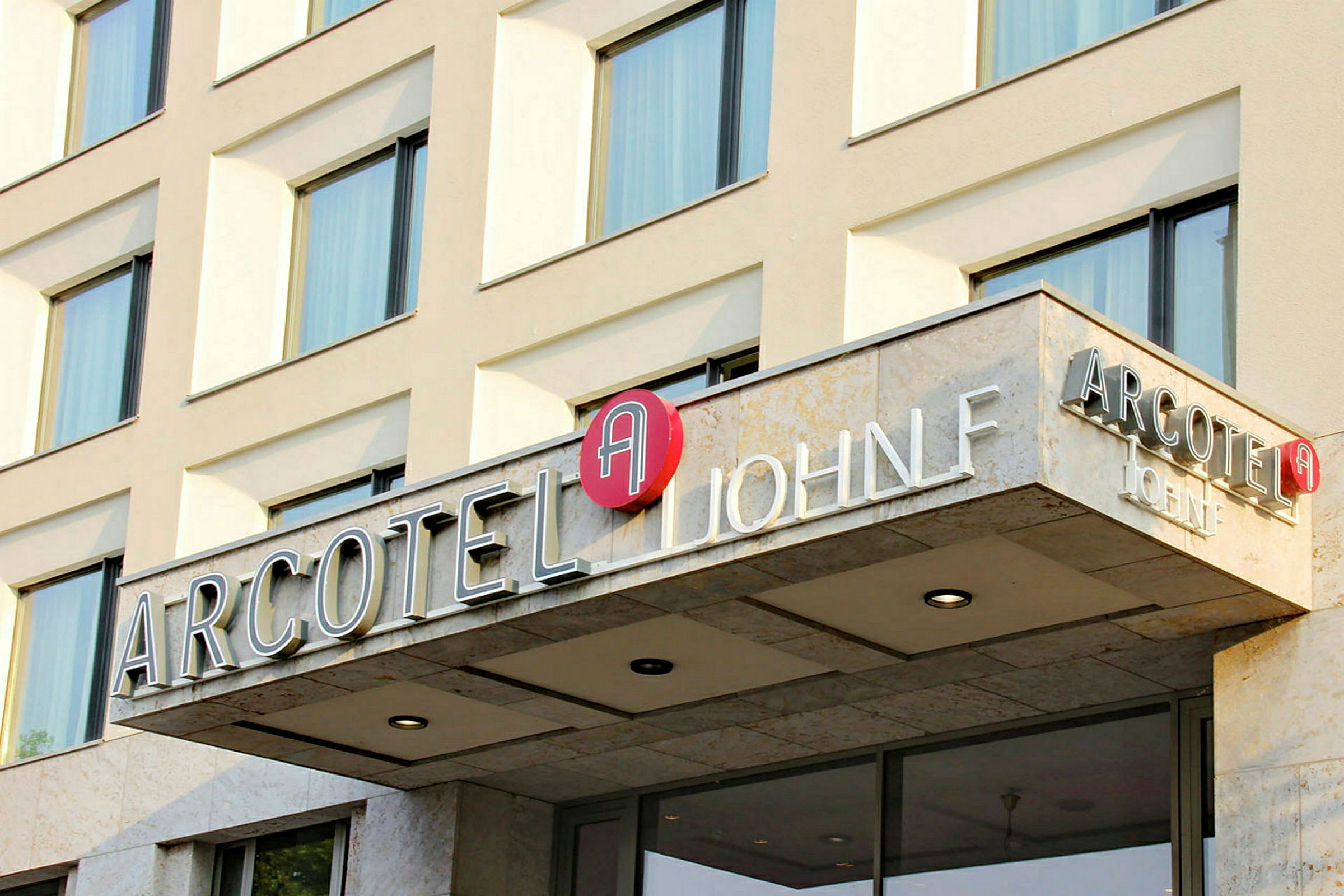 Facade af en hotelbygning med skiltet "Arcotel John F". (AI-genereret tekst)