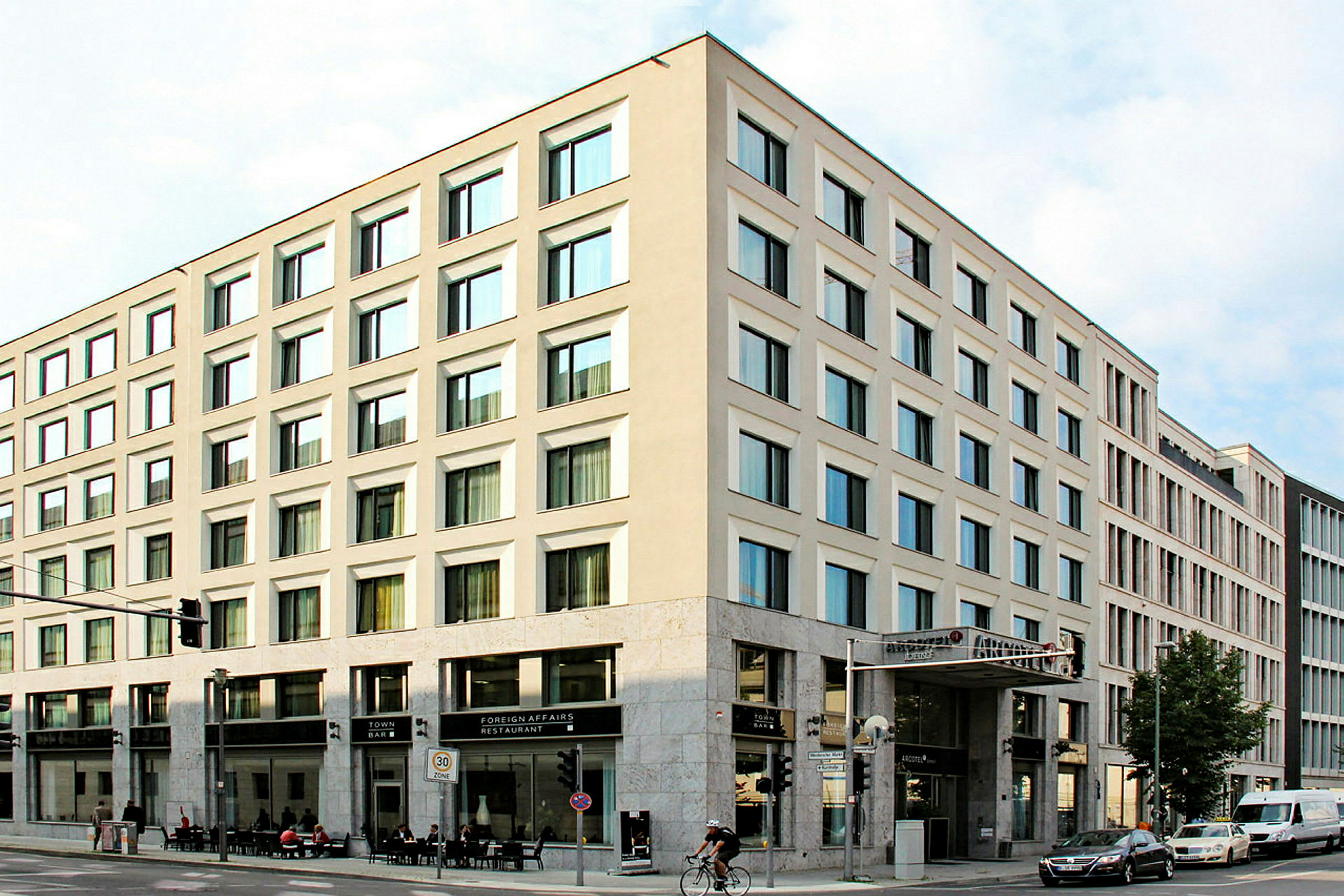 En hjørnebygning med moderne facader og store vinduer, med restaurant og bar i stueetagen. (AI-genereret tekst)