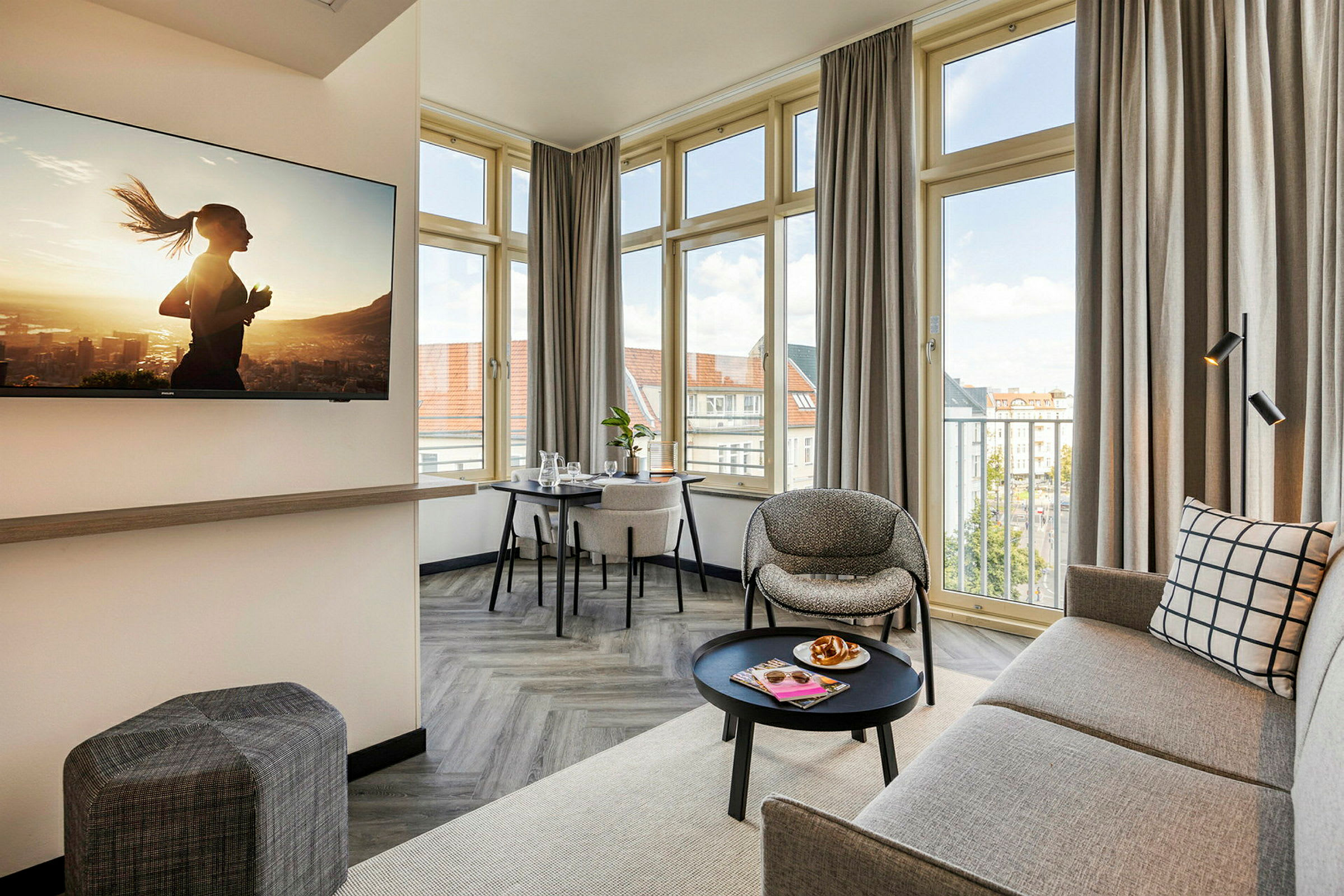 En moderne og lys hotelsuite med sofa, lænestol, bord og et tv på væggen. (AI-genereret tekst)