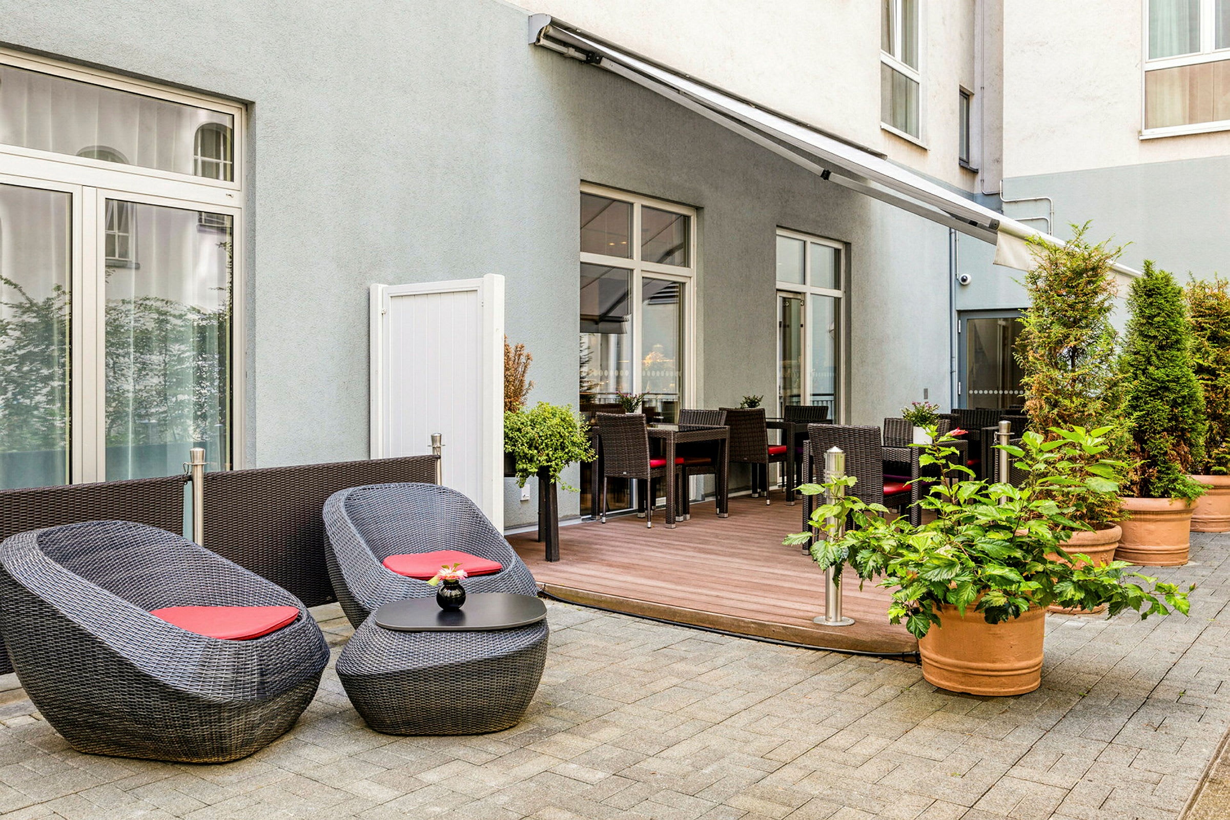 Udendørs terrasse med borde, stole og siddepladser omgivet af blomsterpotter. (AI-genereret tekst)