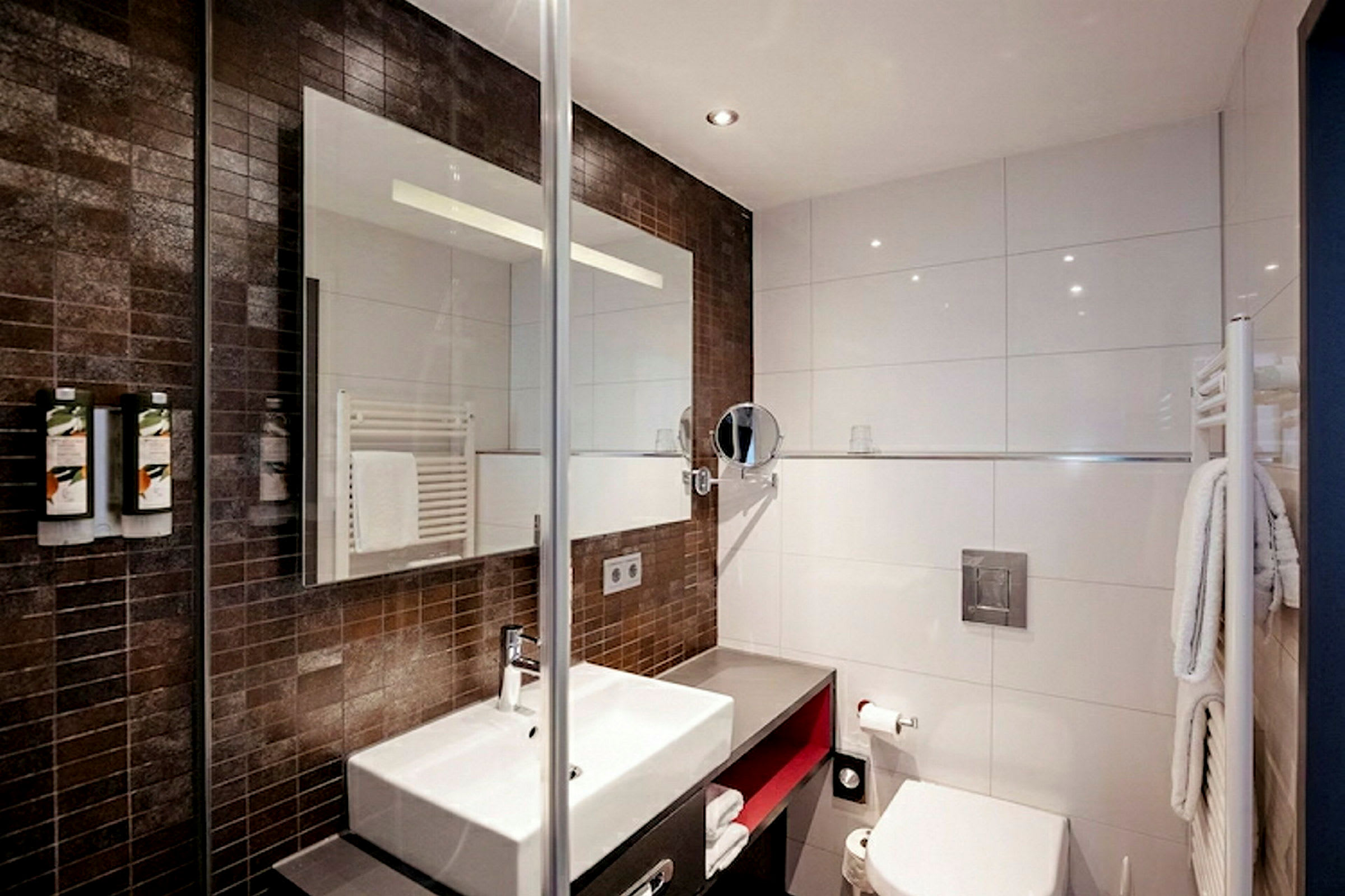 Moderne badeværelse med brun mosaik og hvide vægge, håndvask, spejl og toilet. (AI-genereret tekst)