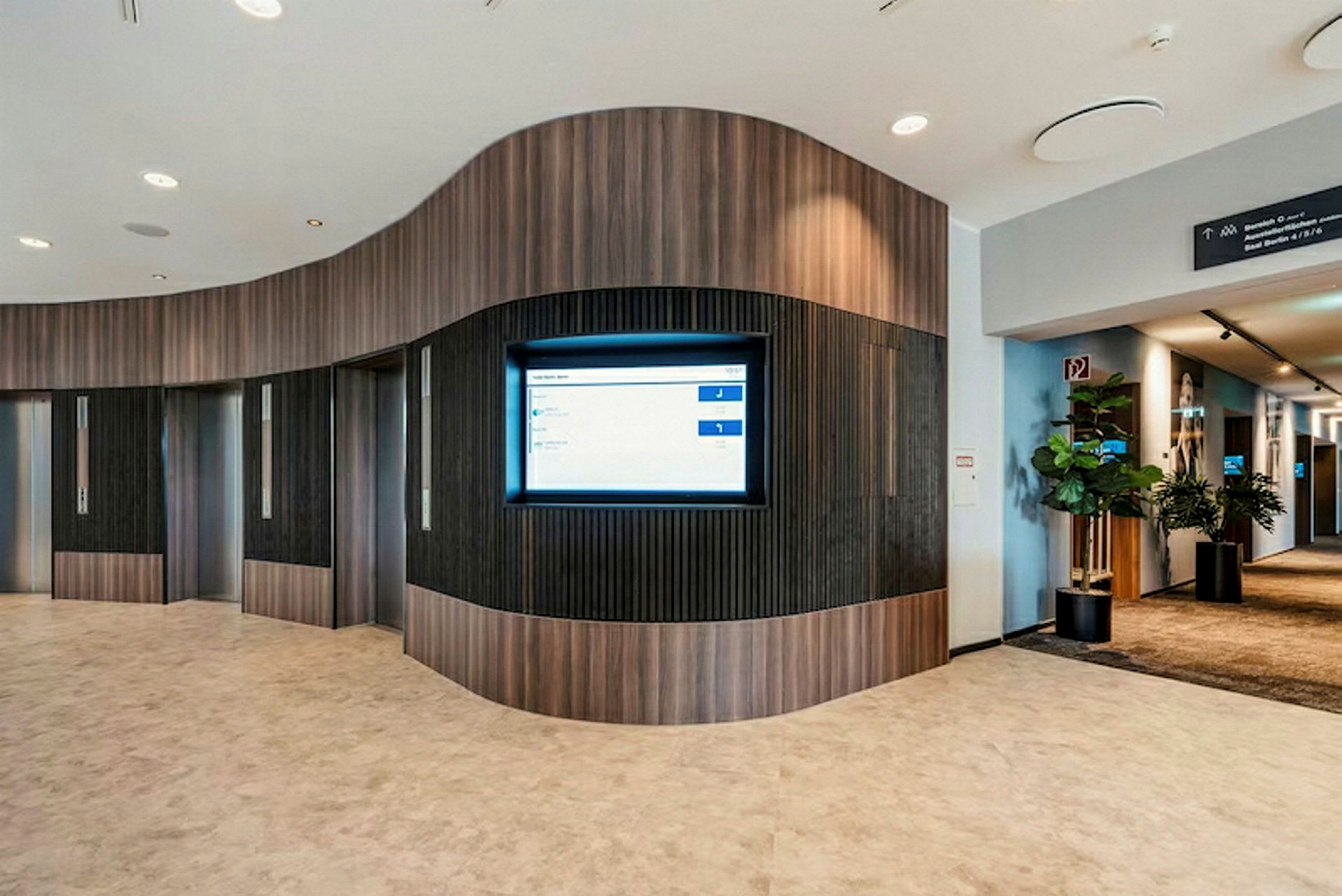 Interiør af en moderne lobby med elevatorer og en informationsskærm på væggen. (AI-genereret tekst)