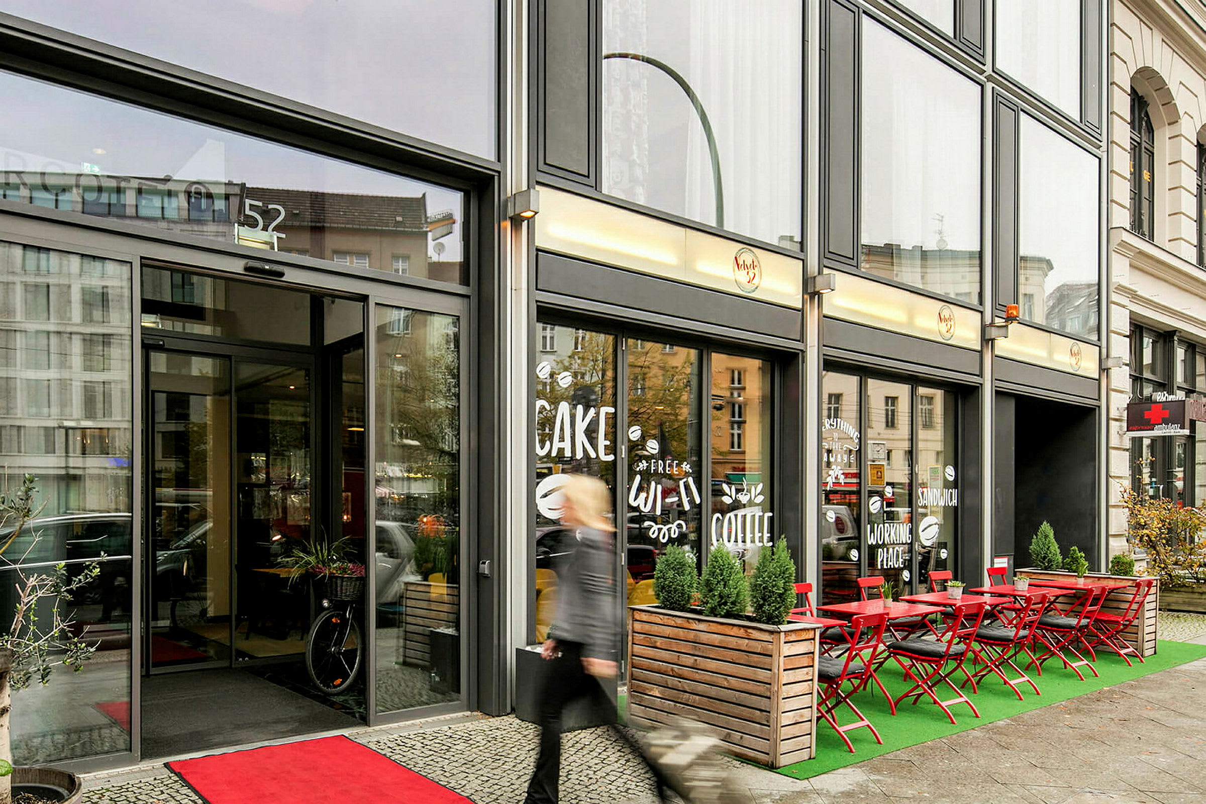 Indgangen til en cafébygning med udendørsservering og skilte i vinduet. (AI-genereret tekst)