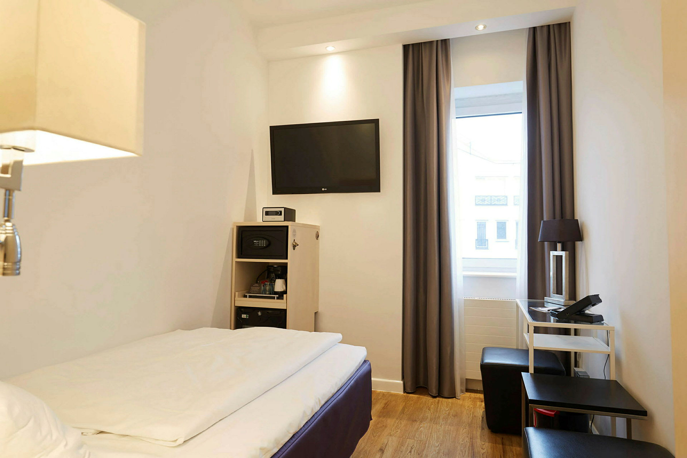 Et hotelværelse med en seng, TV på væggen og møbler såsom et skrivebord og stol. (AI-genereret tekst)