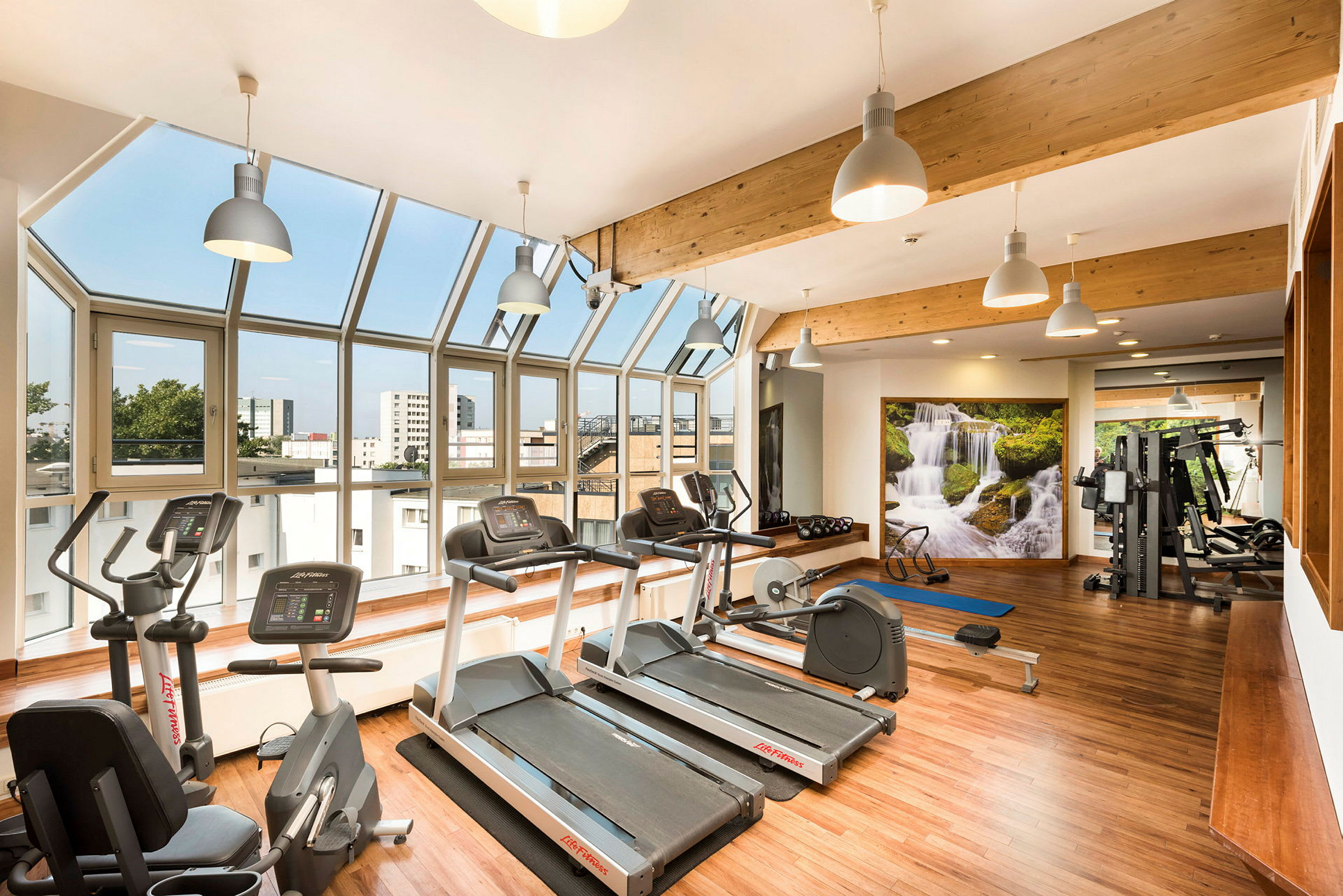 Et træningscenter med fitnessmaskiner, lys indretning og store vinduer. (AI-genereret tekst)