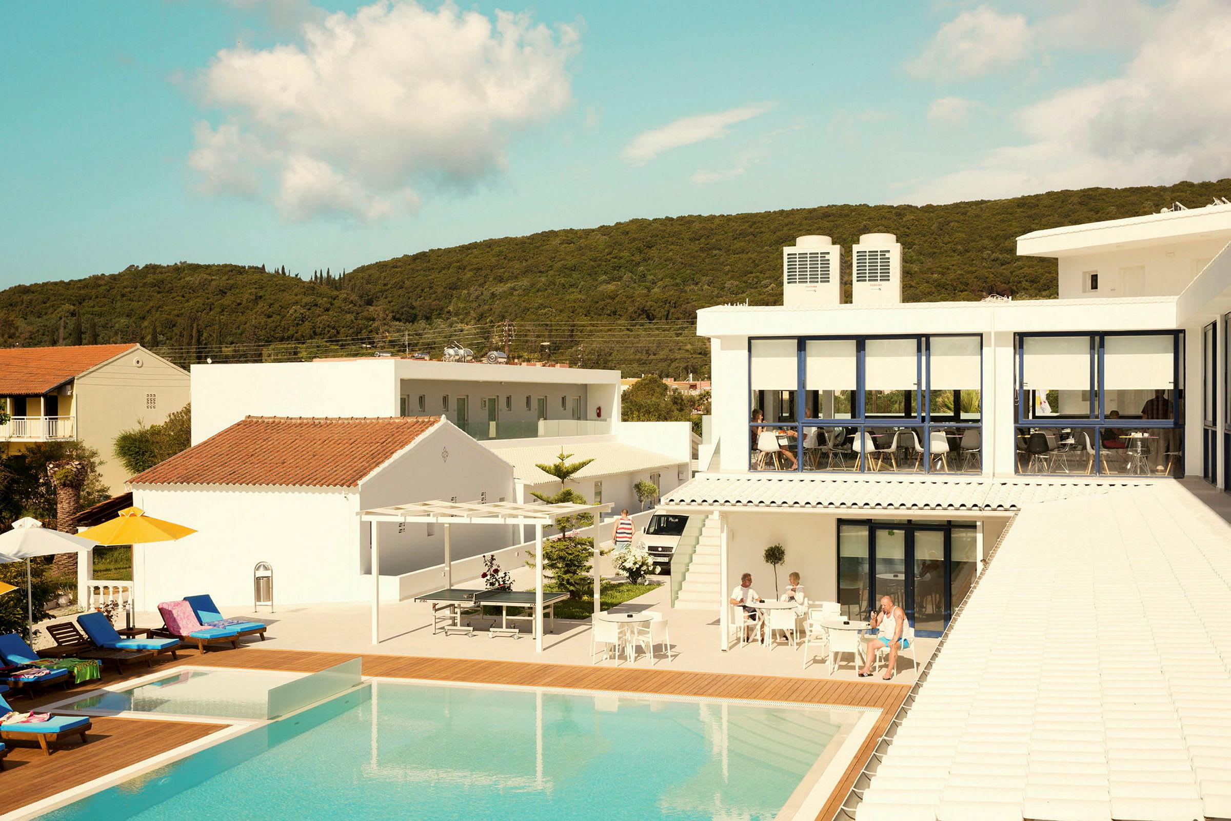 Et hotel med en pool og liggestole, omgivet af bygninger og natur. (AI-genereret tekst)