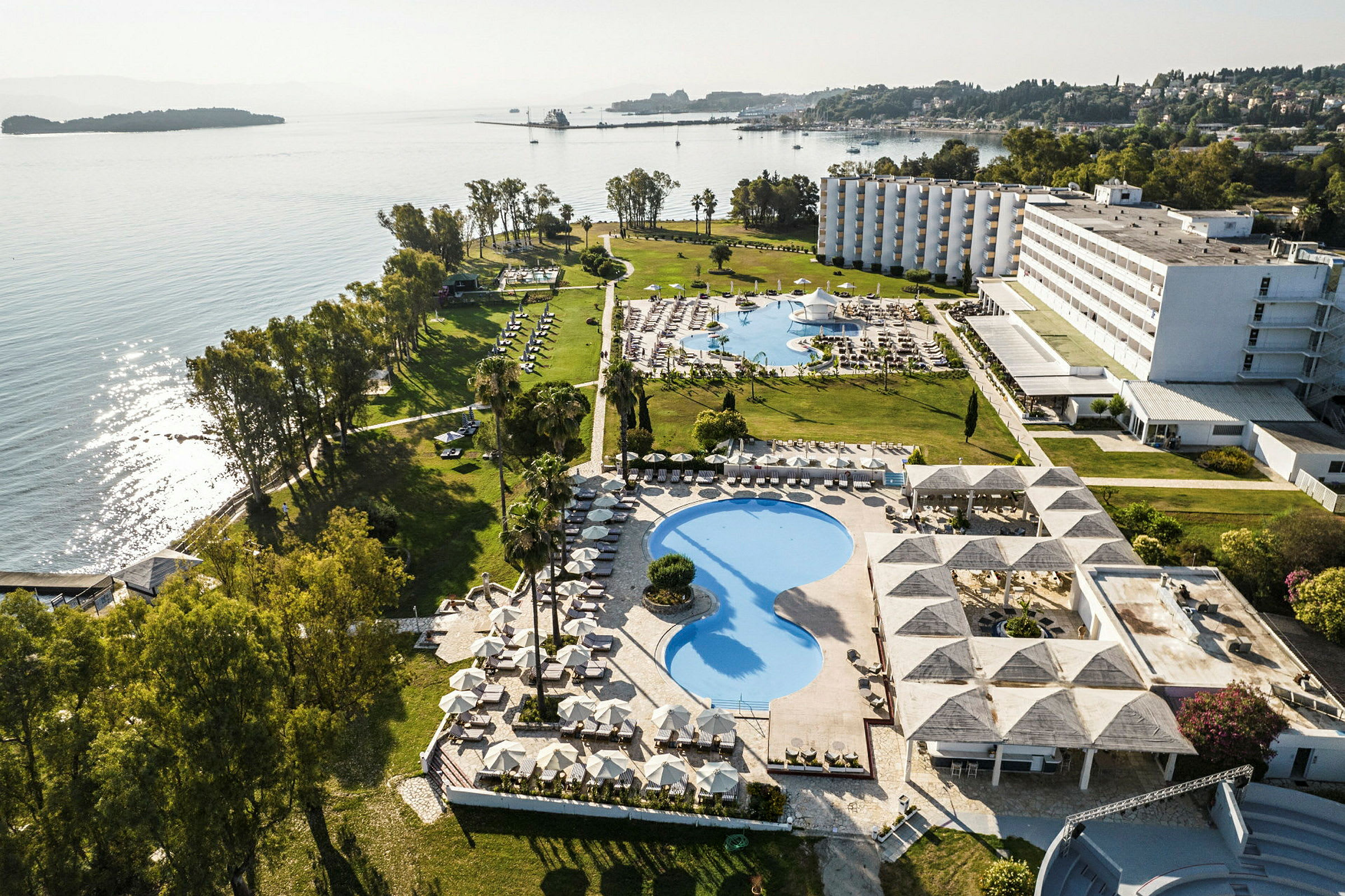 Luftfoto af et hotelområde ved havet med swimmingpools, grønne områder og bygninger. (AI-genereret tekst)