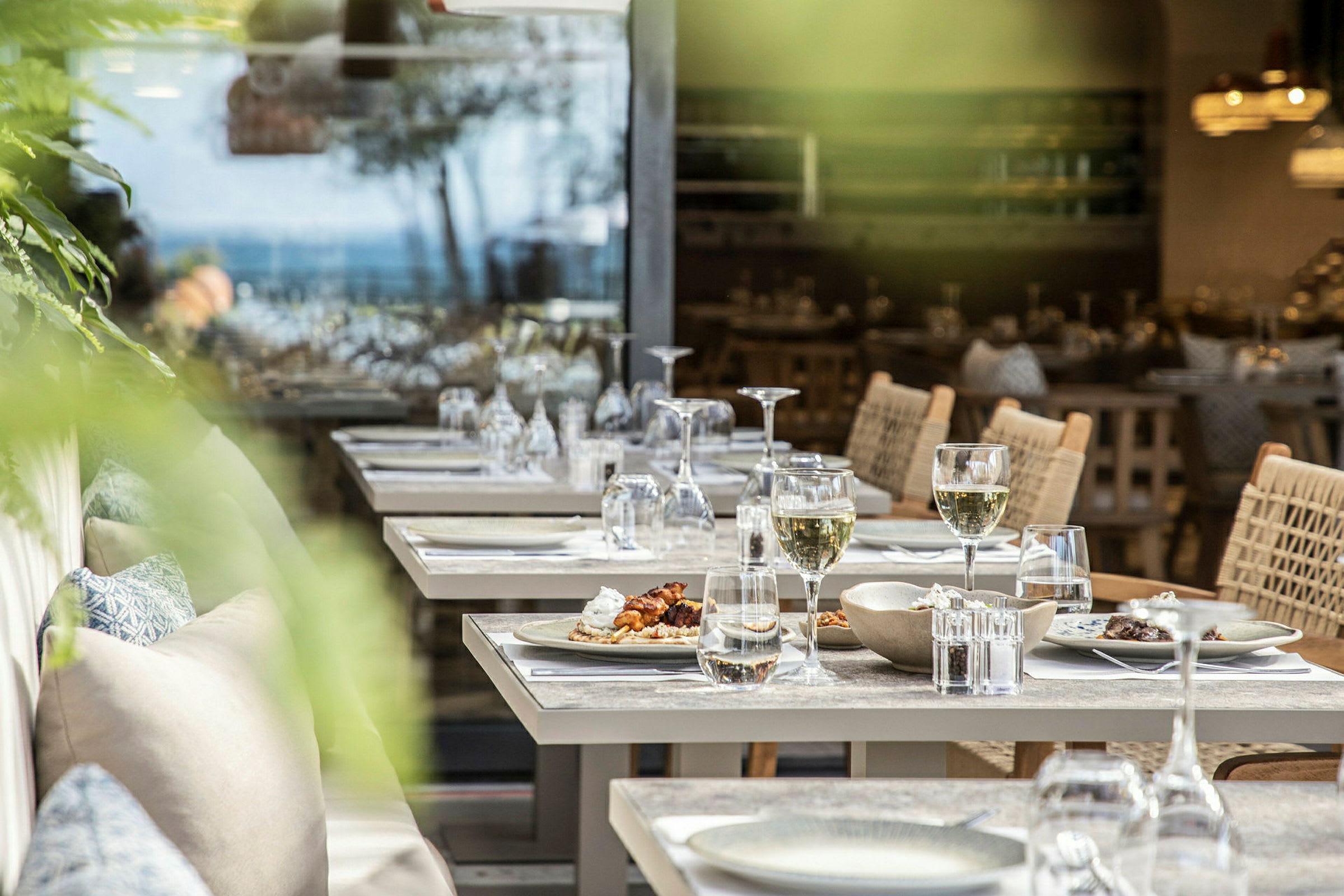 Billede af opdækkede borde på en restaurant med tallerkener, glas og stole. (AI-genereret tekst)