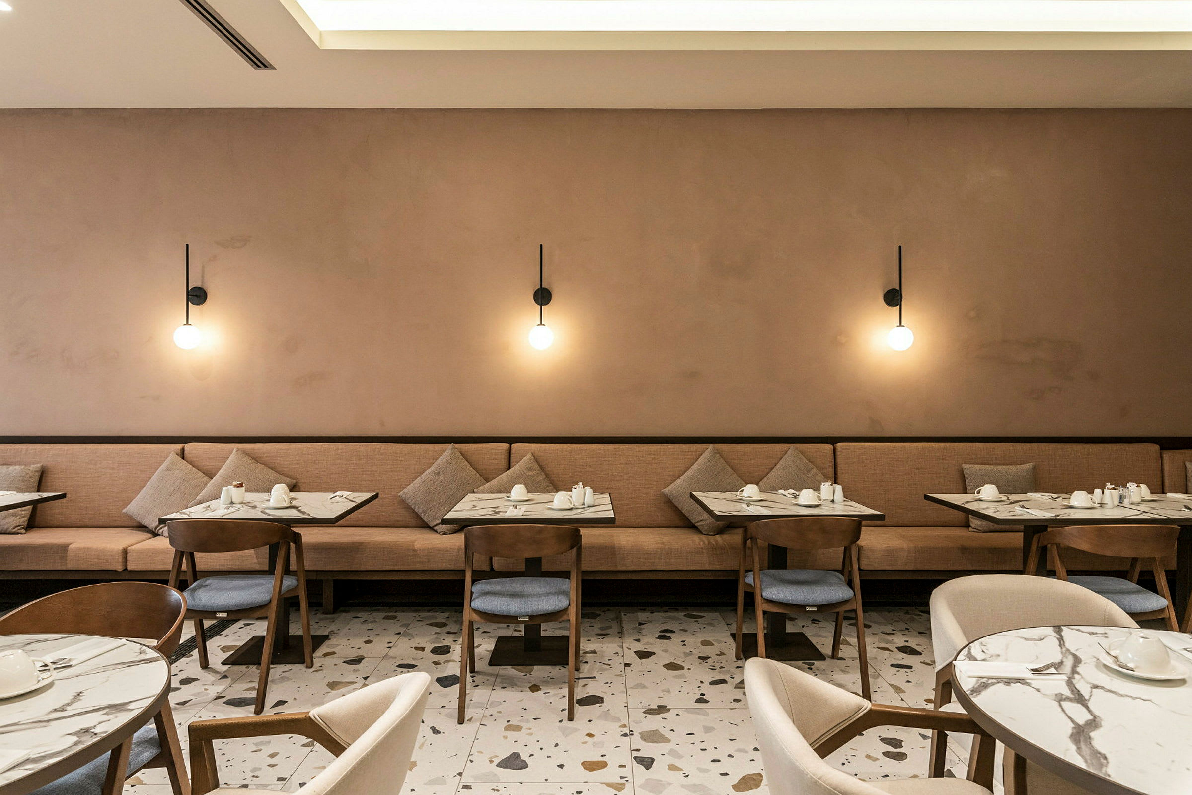 Restaurant med borde og stole, samt beige sofa og væglamper. (AI-genereret tekst)