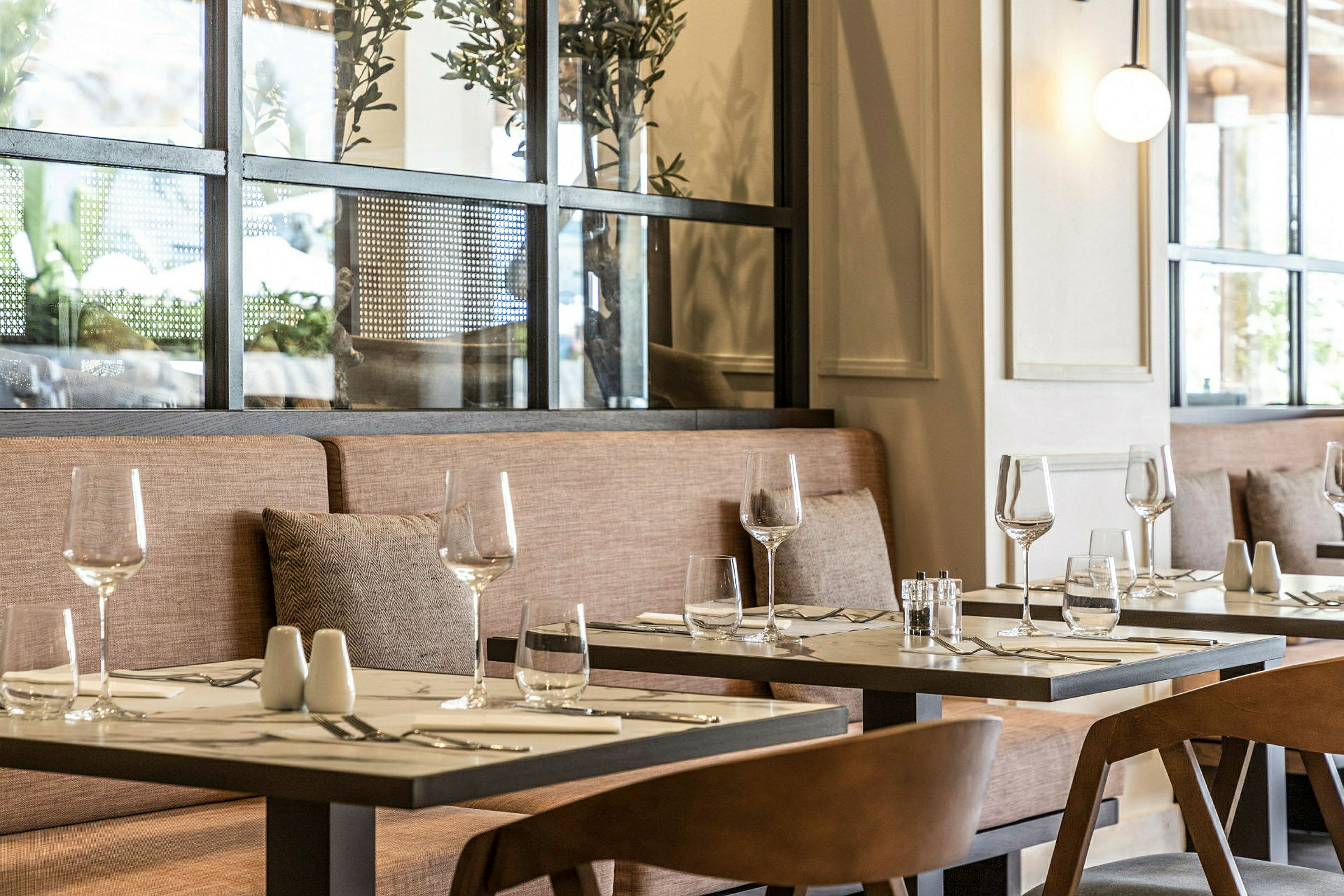 Et restaurantbord med glas og bestik på en dug, omgivet af stole og en sofa med puder. (AI-genereret tekst)
