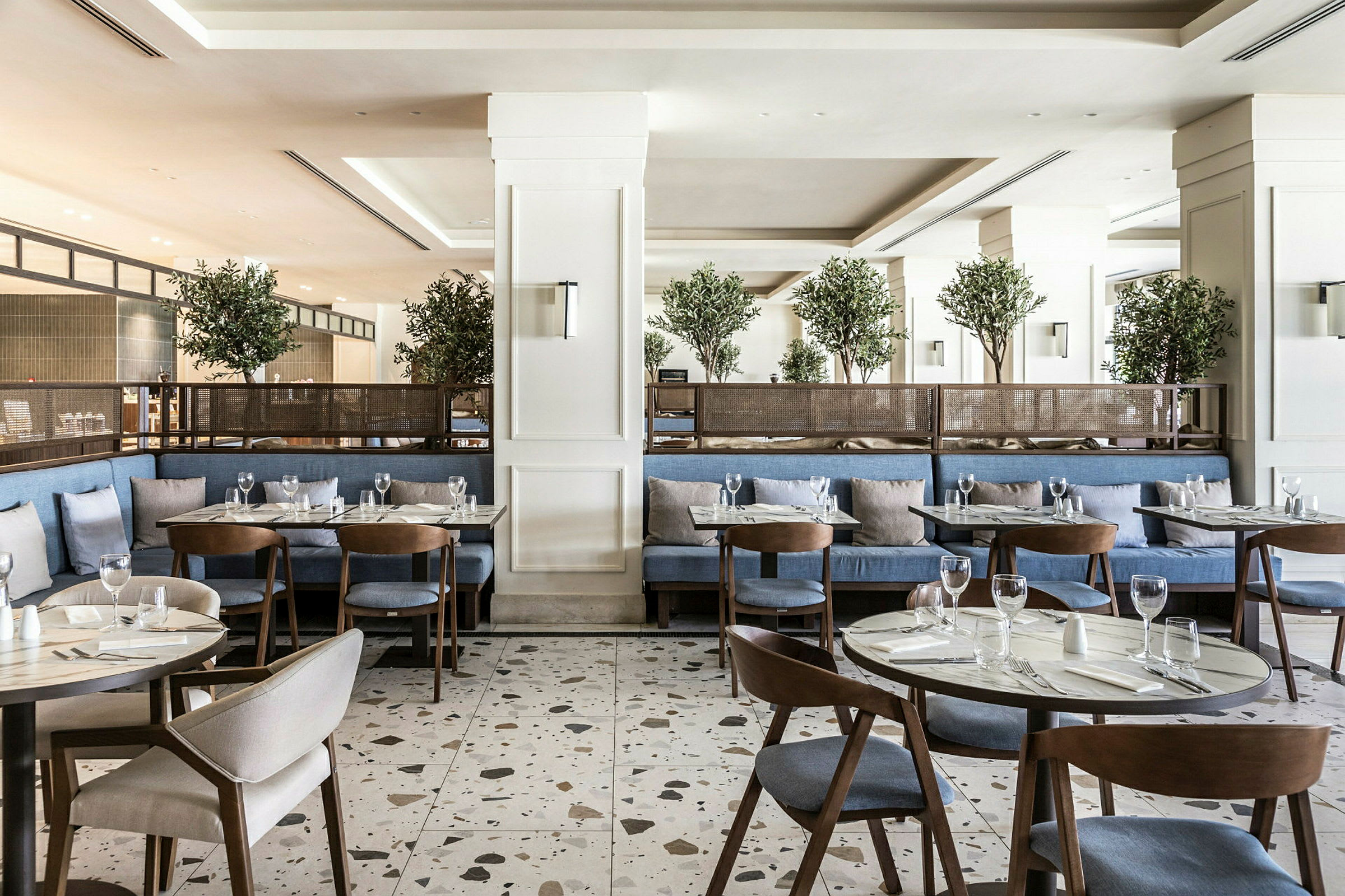En moderne restaurant med blå siddepladser, træborde og grønne planter som dekoration. (AI-genereret tekst)