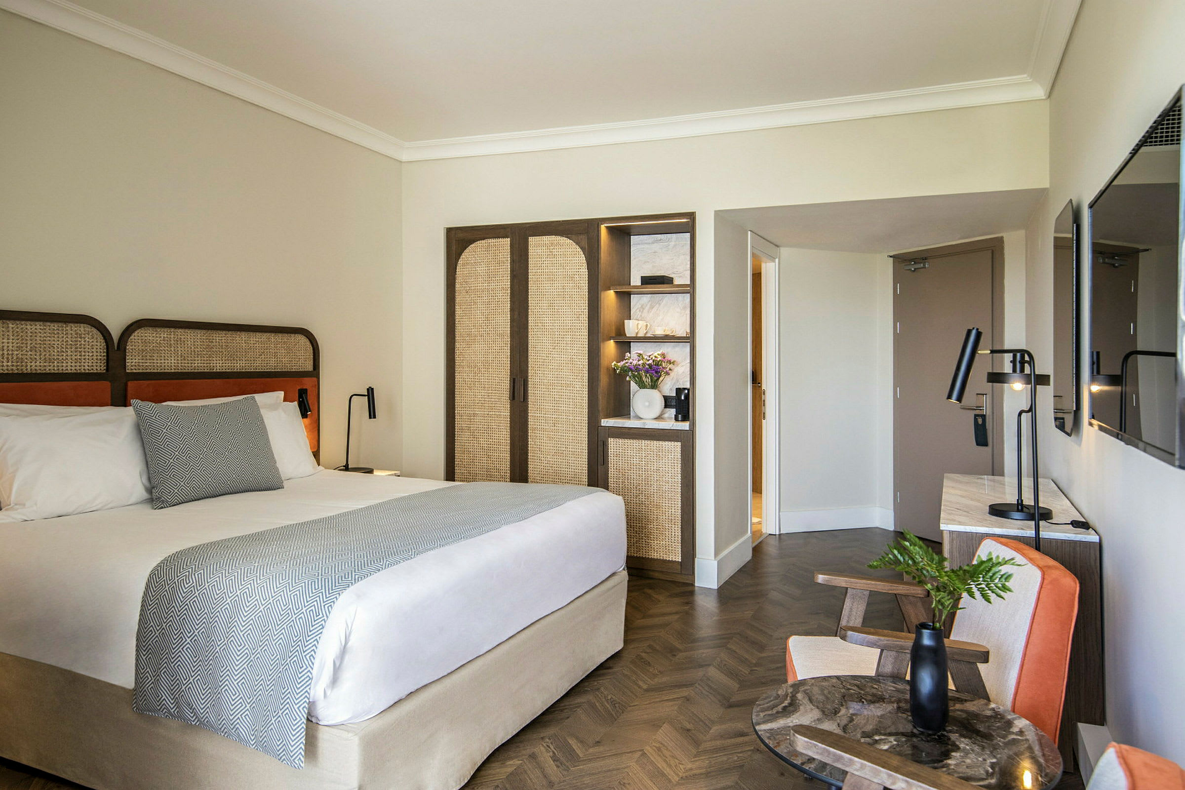Et moderne hotelværelse med en dobbeltseng, et klædeskab med indbyggede hylder og et bord med stole. (AI-genereret tekst)