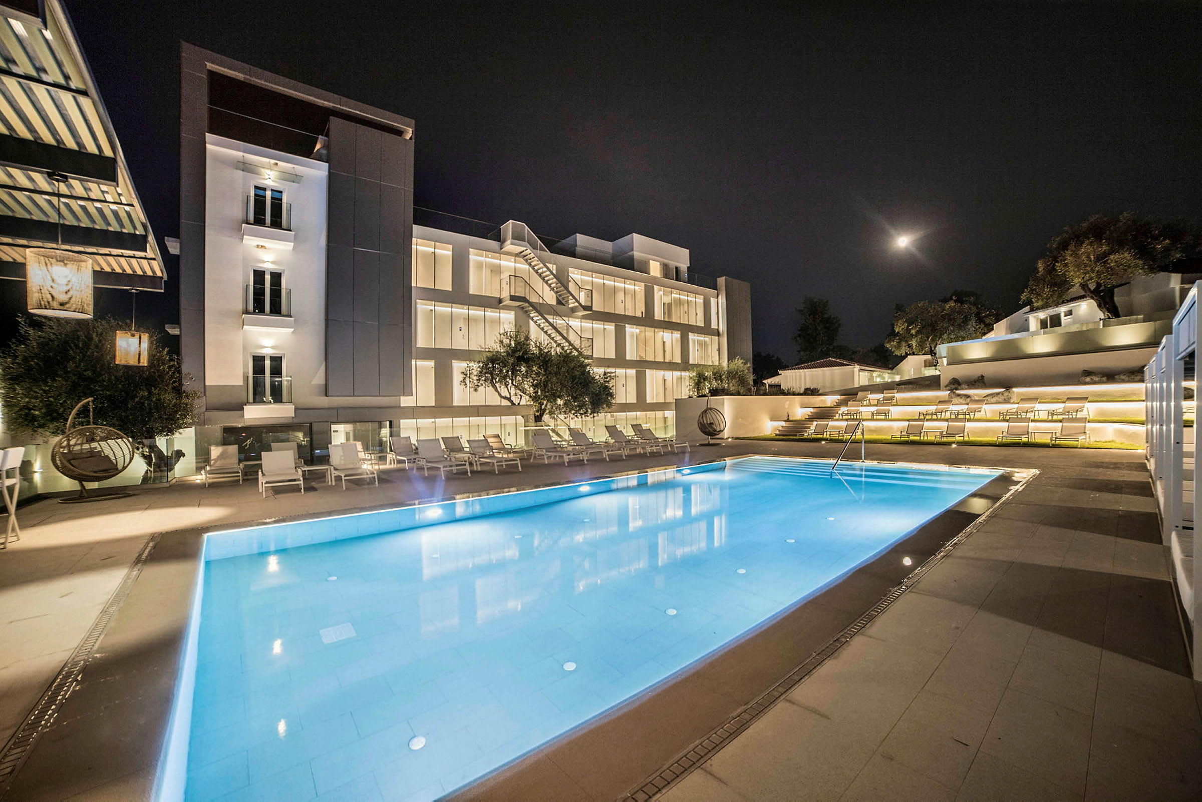 Et hotel med en oplyst swimmingpool foran bygningen om aftenen. (AI-genereret tekst)