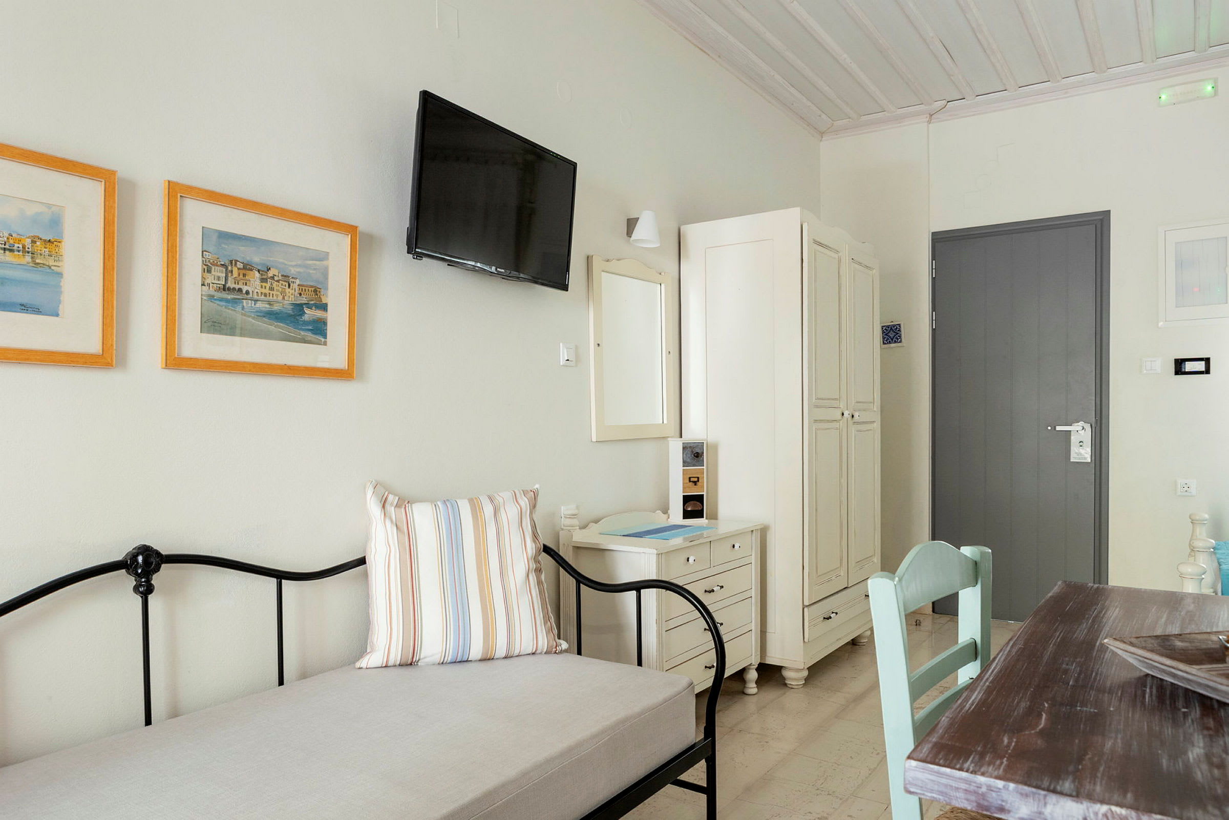 Et lyst og enkelt møbleret hotelværelse med en dør, garderobe, billeder og bord. (AI-genereret tekst)