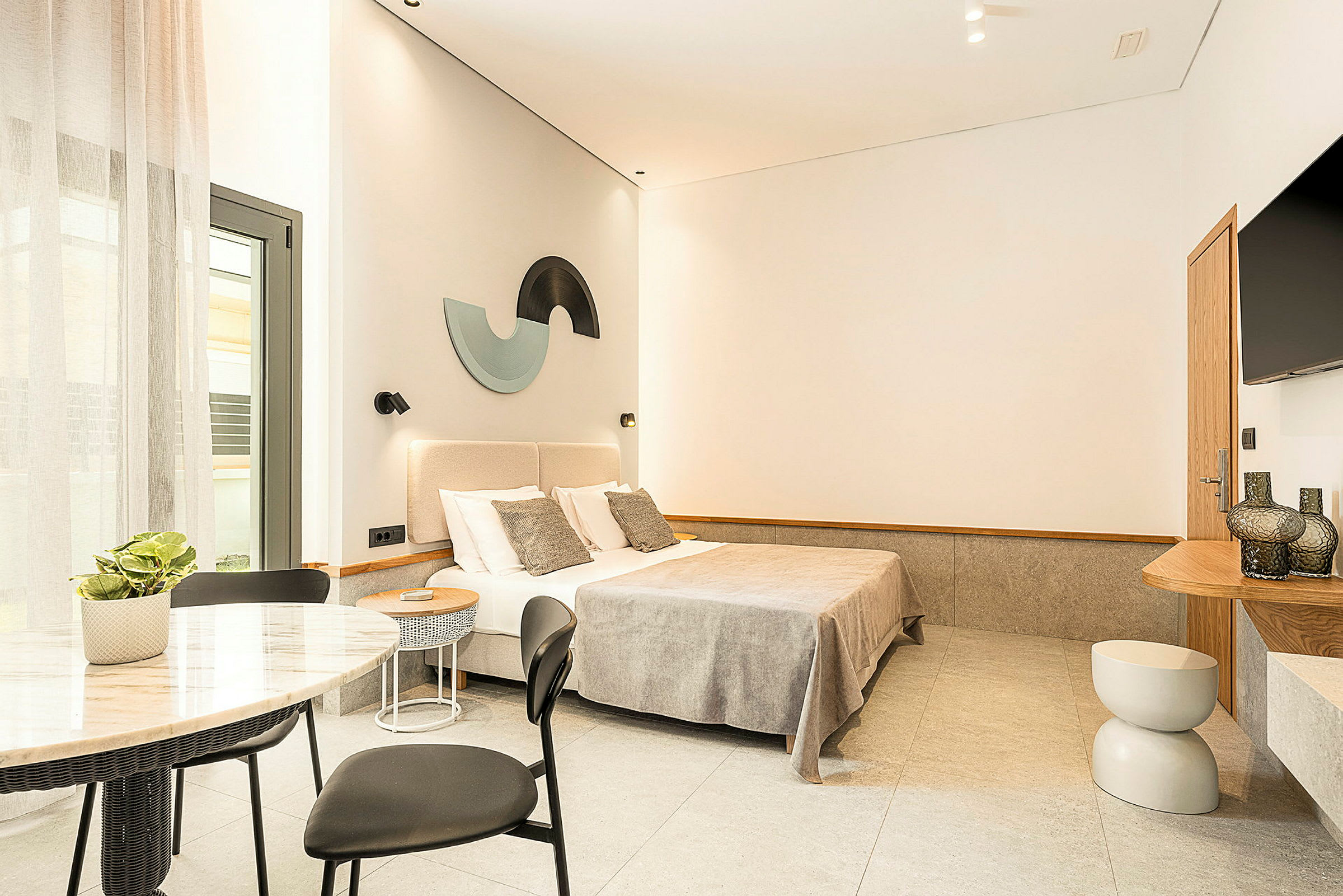 Et moderne og stilrent hotelværelse med en dobbeltseng, garderobe, bord med stole samt dekorationer på væggene. (AI-genereret tekst)
