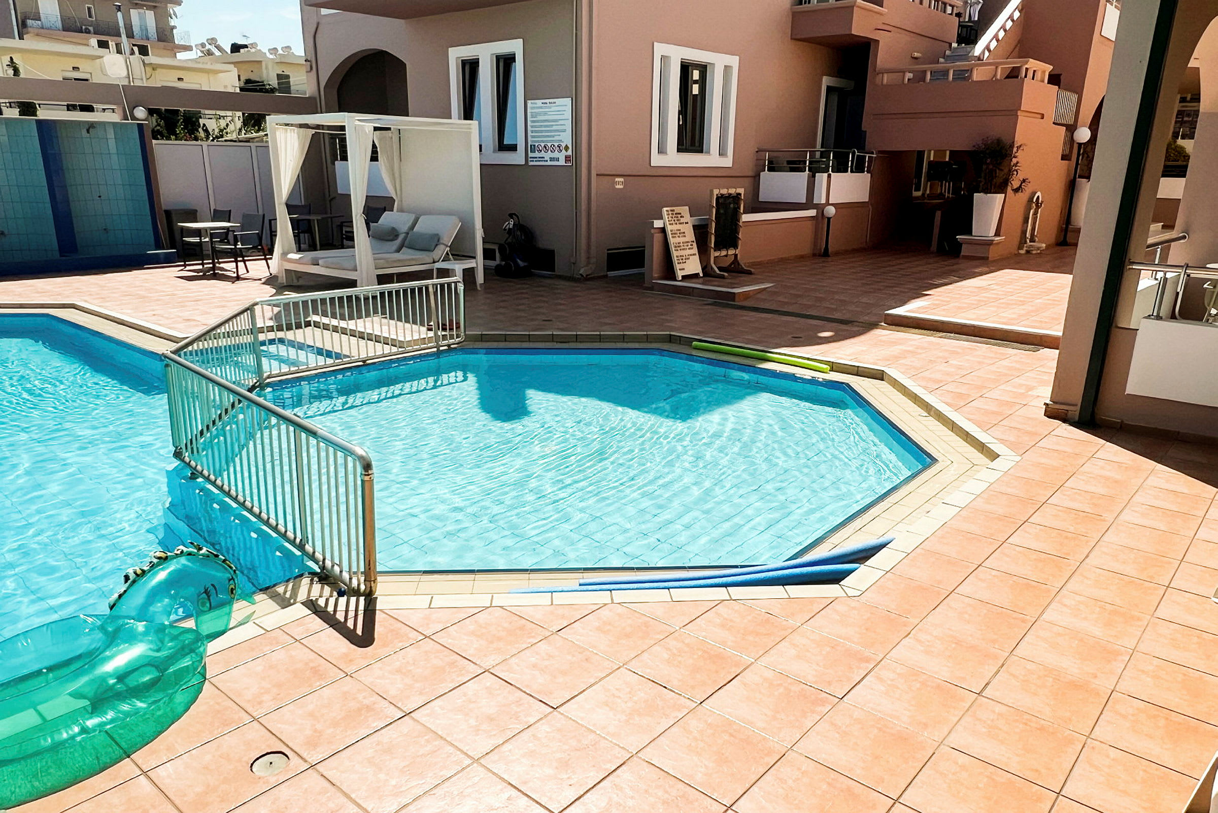 Udendørs swimmingpool med hegn, omgivet af et flisebelagt område og solsenge. (AI-genereret tekst)