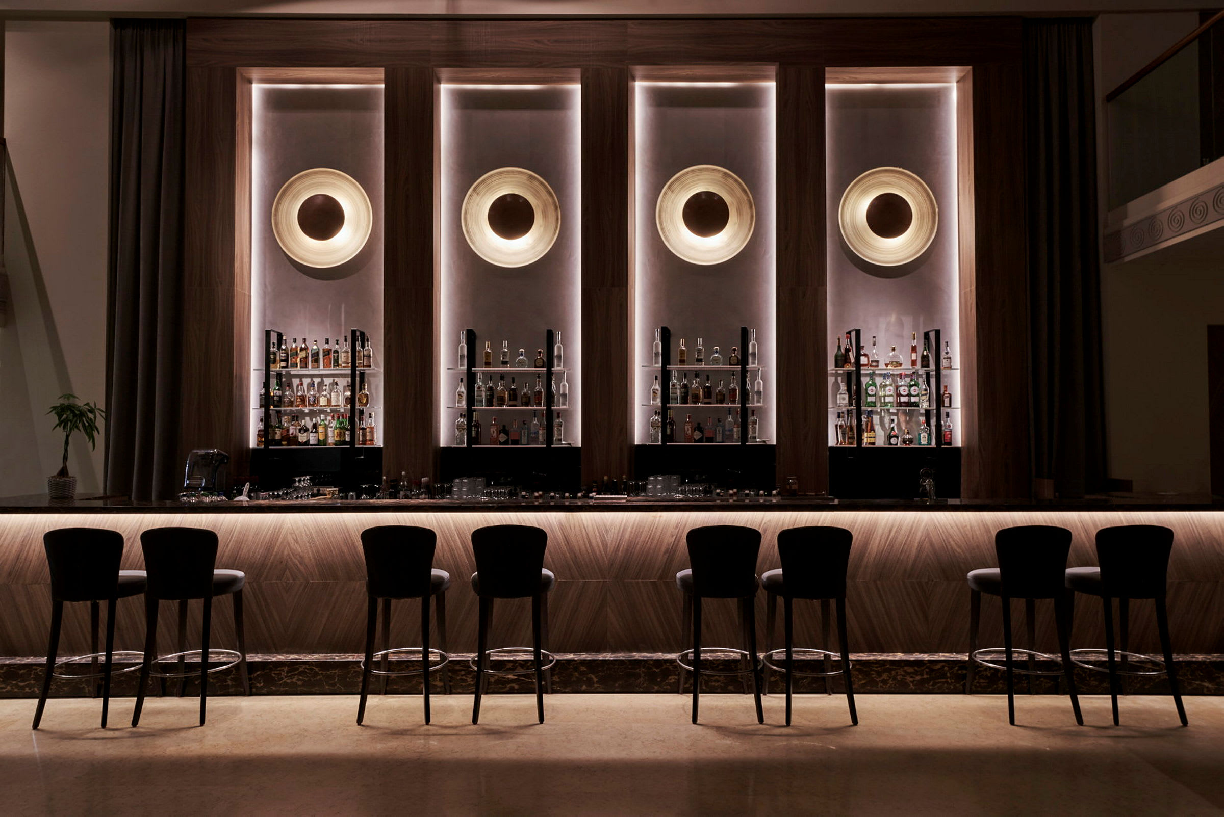 Elegant hotelbar med høje stole og flasker opstillet bag baren. (AI-genereret tekst)