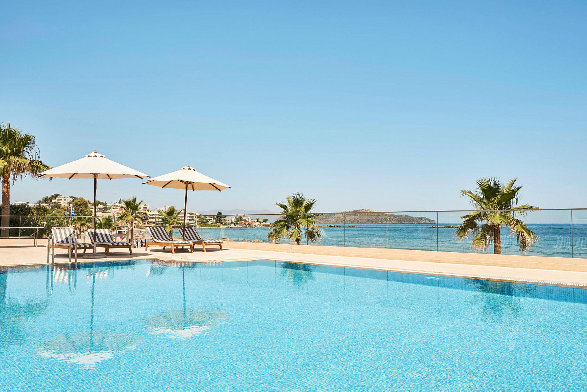 En udendørs swimmingpool med parasoller og liggestole, beliggende ved havet. (AI-genereret tekst)