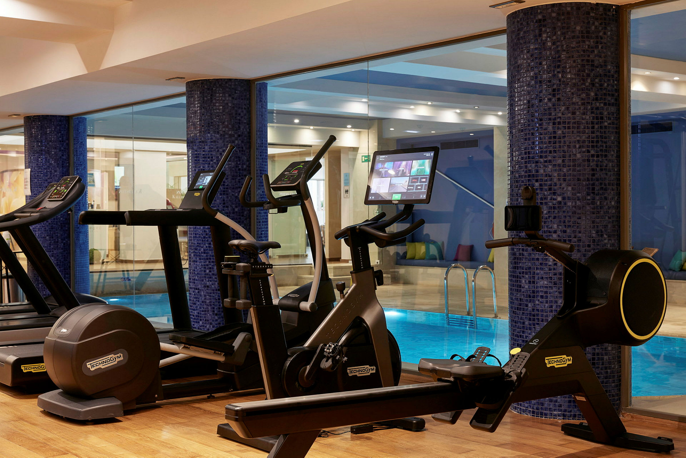Fitnessudstyr foran en glasvæg med udsigt til en pool. (AI-genereret tekst)