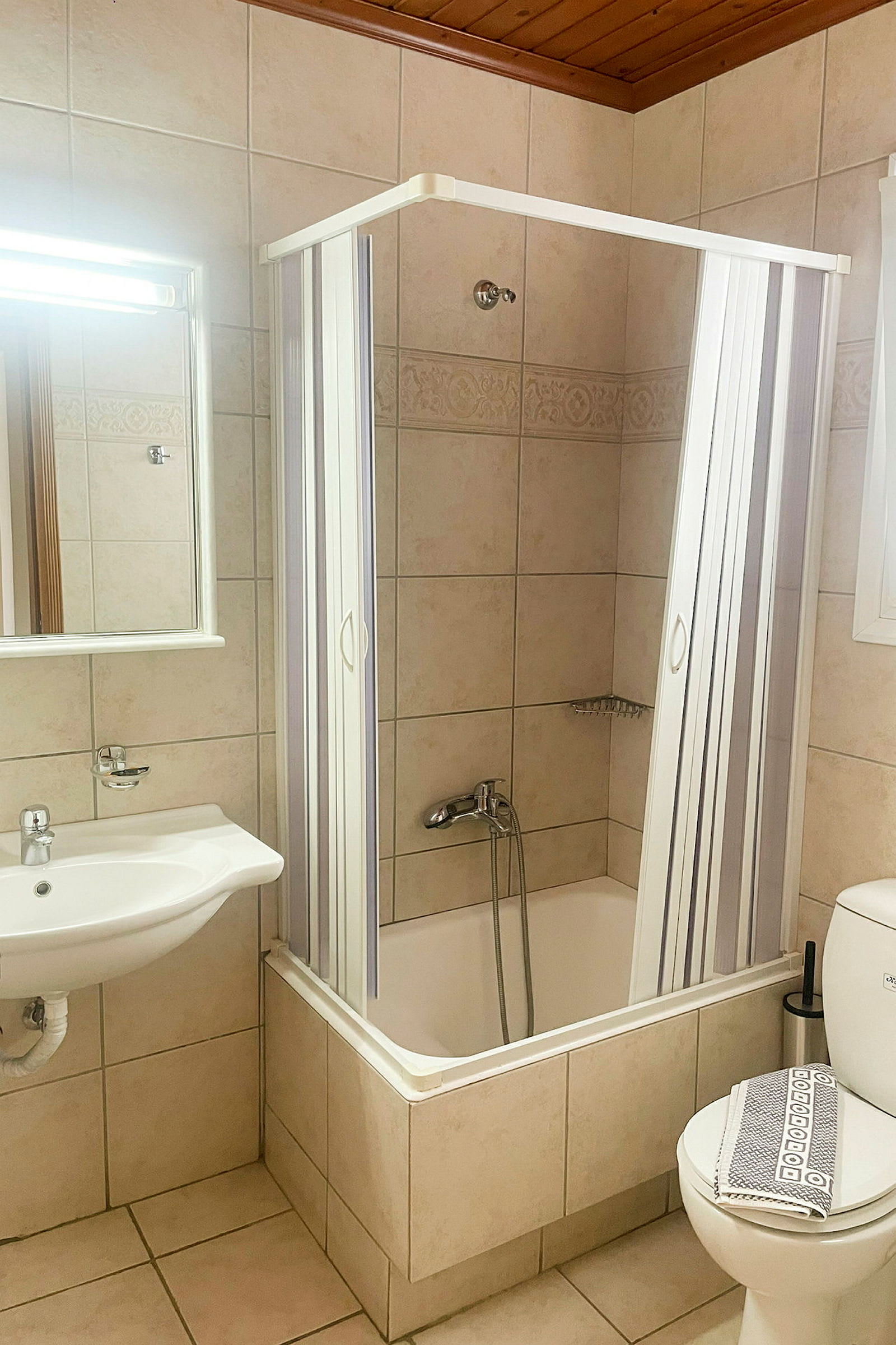 Et badeværelse med brusekabine og badekar, håndvask med spejl og toilet. (AI-genereret tekst)