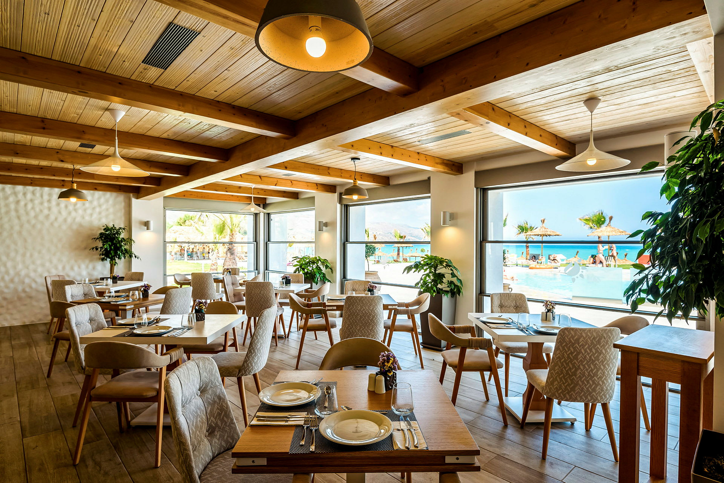 En restaurant med borde og stole indendørs og udsigt over pool og hav gennem vinduerne. (AI-genereret tekst)